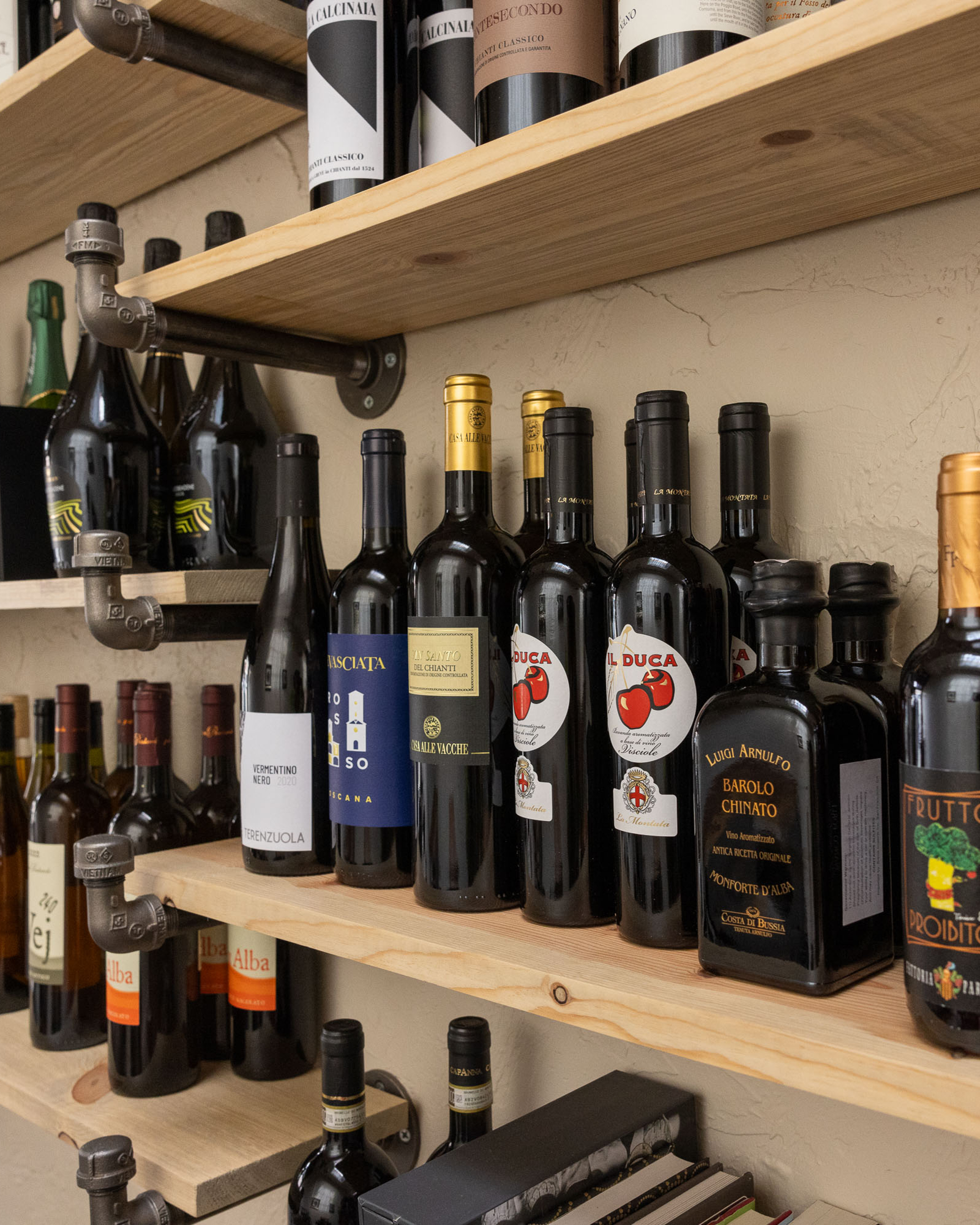 Wooden shelves are mounted on a beige wall, holding an assortment of wine bottles and a few other drink containers, clearly organized for display.