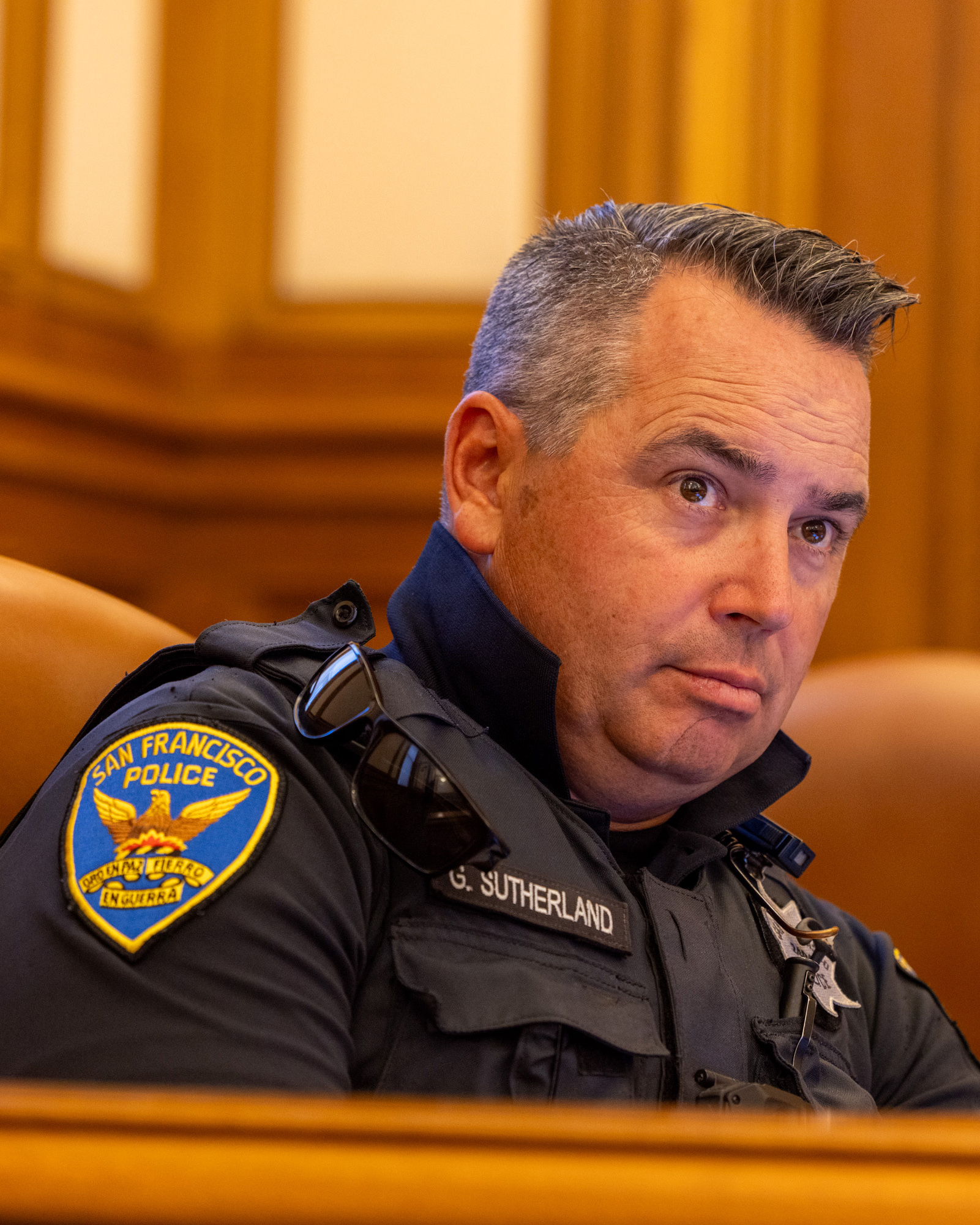 The image shows a stern-looking police officer in uniform, identified by a name tag as G. Sutherland, with a &quot;San Francisco Police&quot; patch on his shoulder.