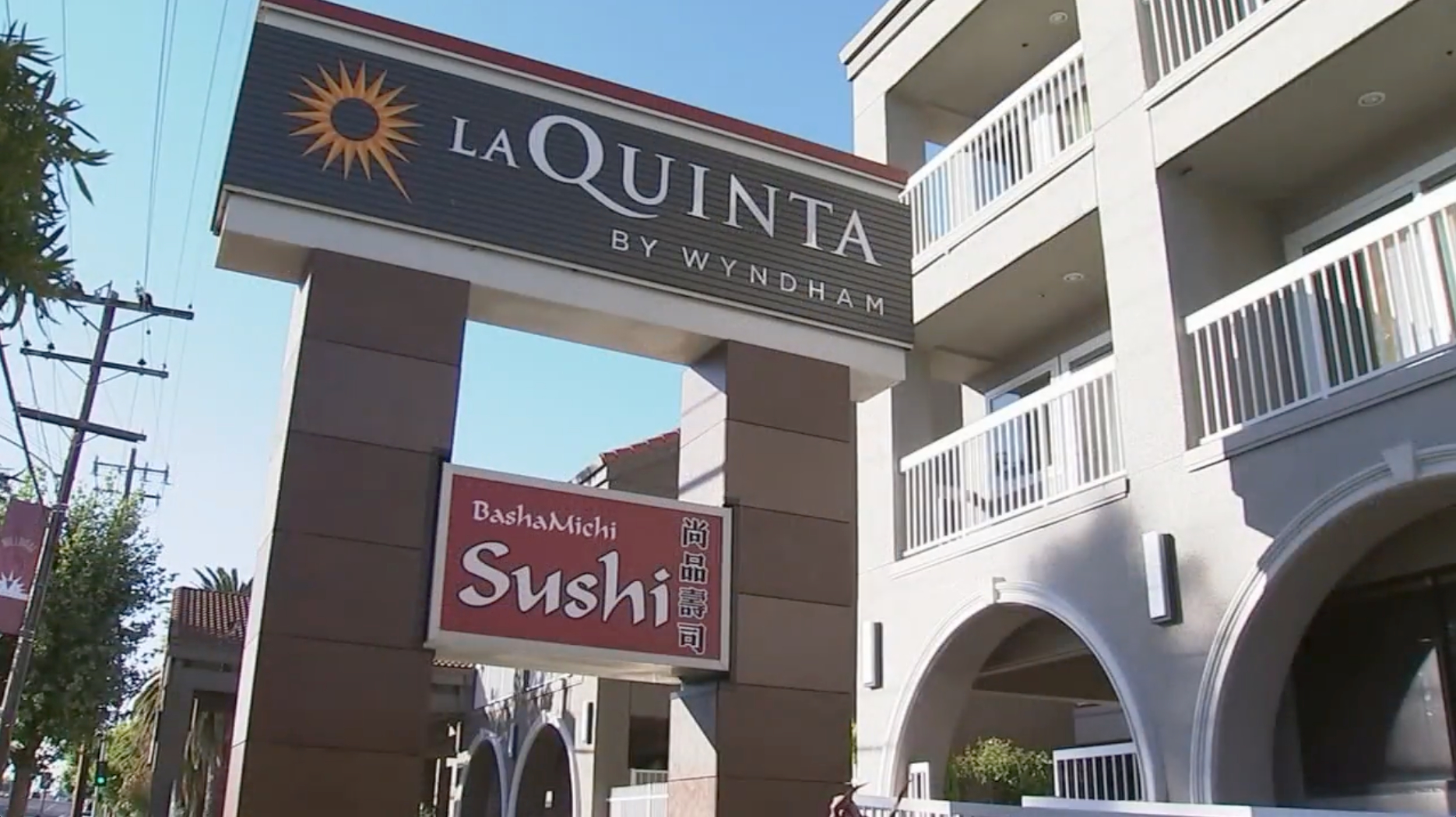 The image shows a La Quinta by Wyndham hotel entrance sign with a sunburst logo and a second sign for &quot;BashaMichi Sushi&quot; restaurant below it.