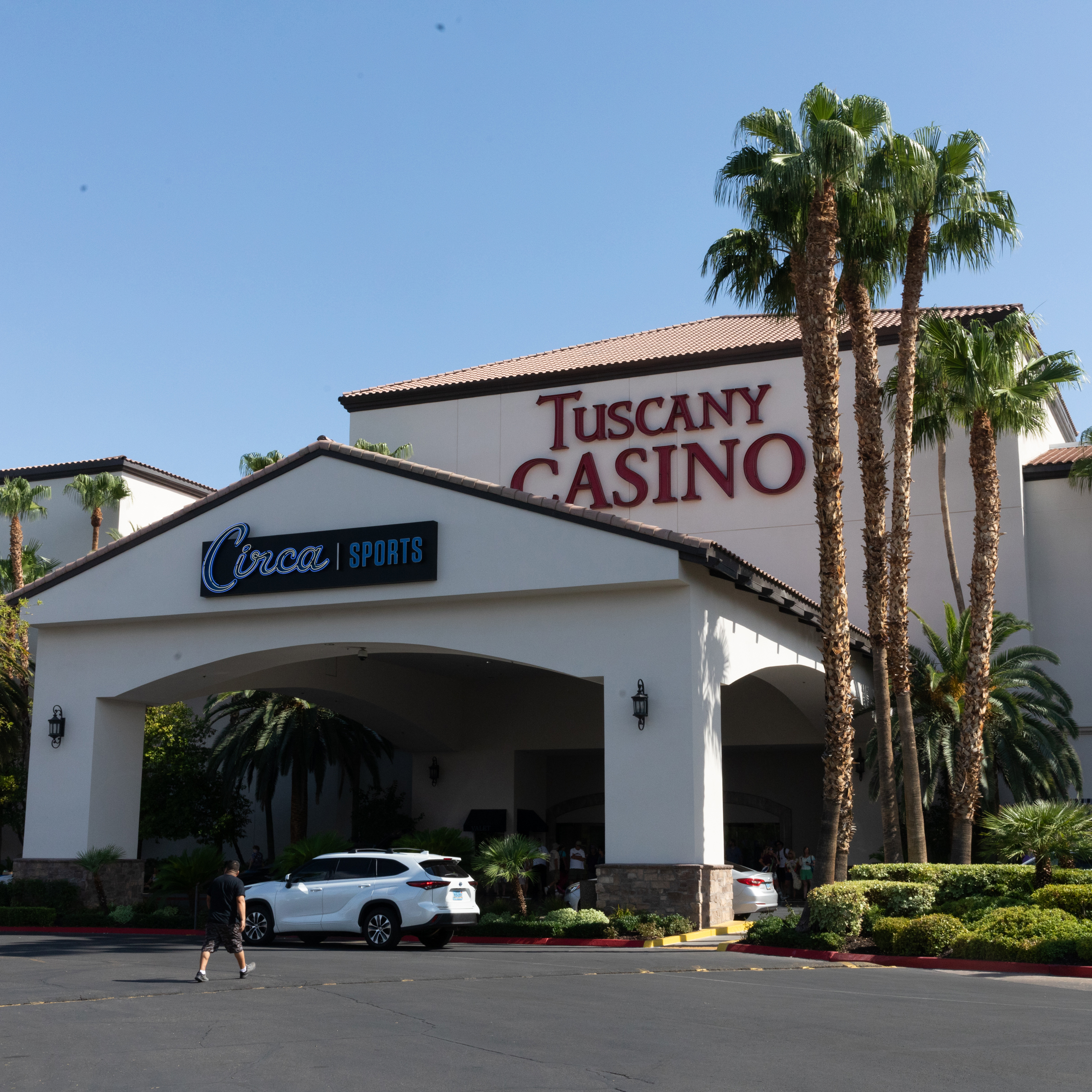 The image shows the entrance to Tuscany Casino, with &quot;Circa Sports&quot; signage above an archway. There are palm trees, parked cars, and a person walking nearby.