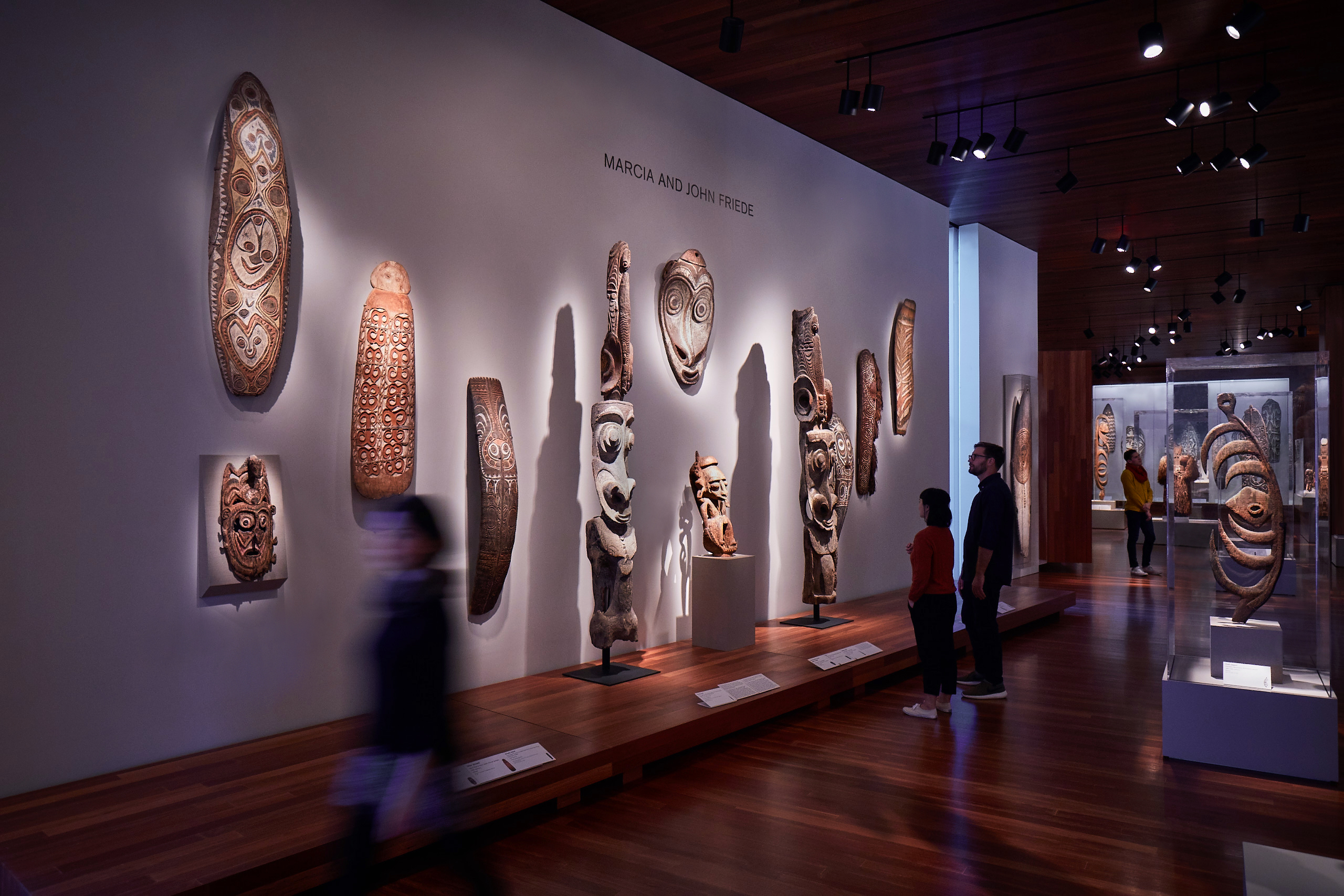 Masks of many types are displayed in soft lighting along a white wall. 