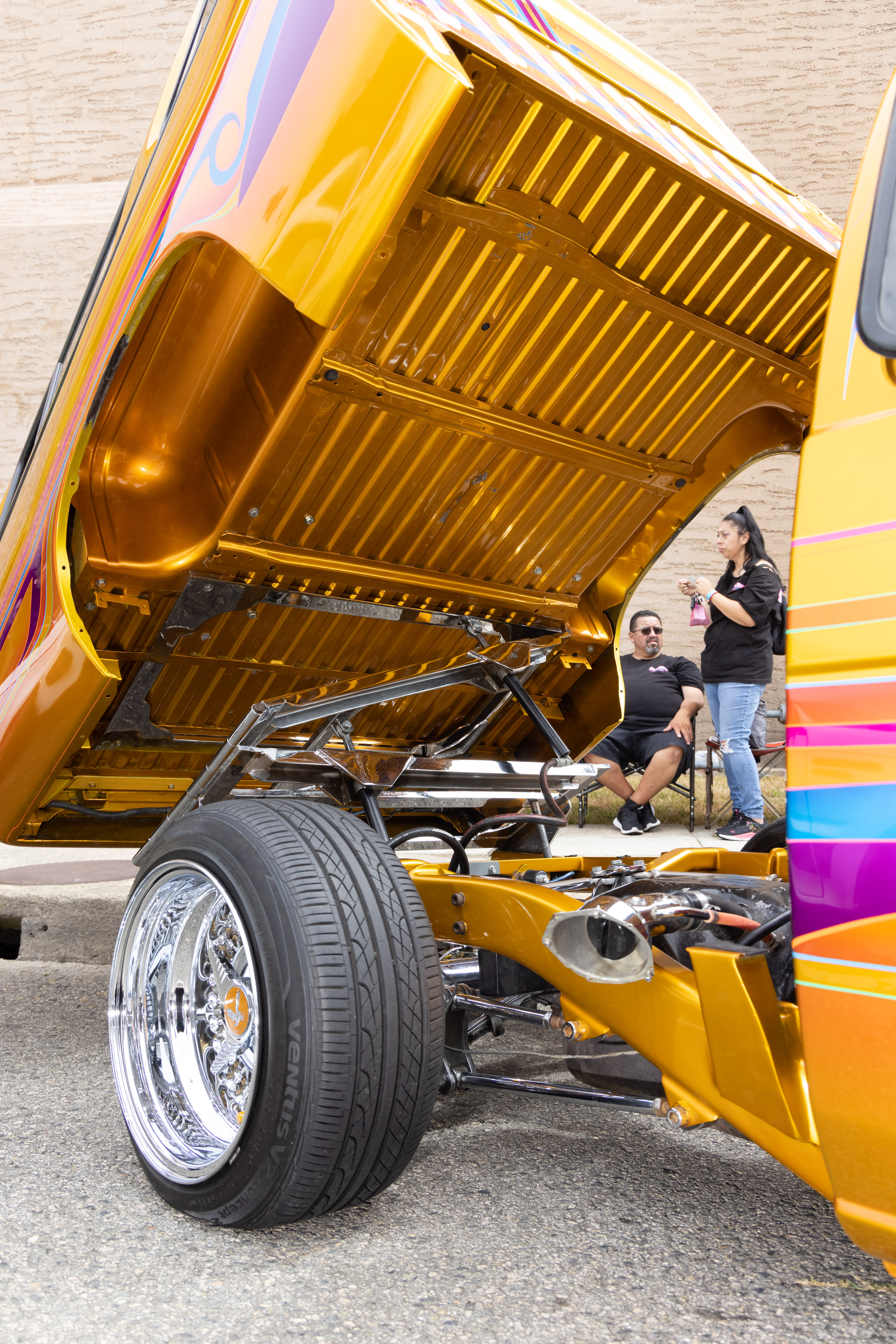 A brightly colored car with its hood open, showcasing intricate detailing. A man and woman conversing nearby.