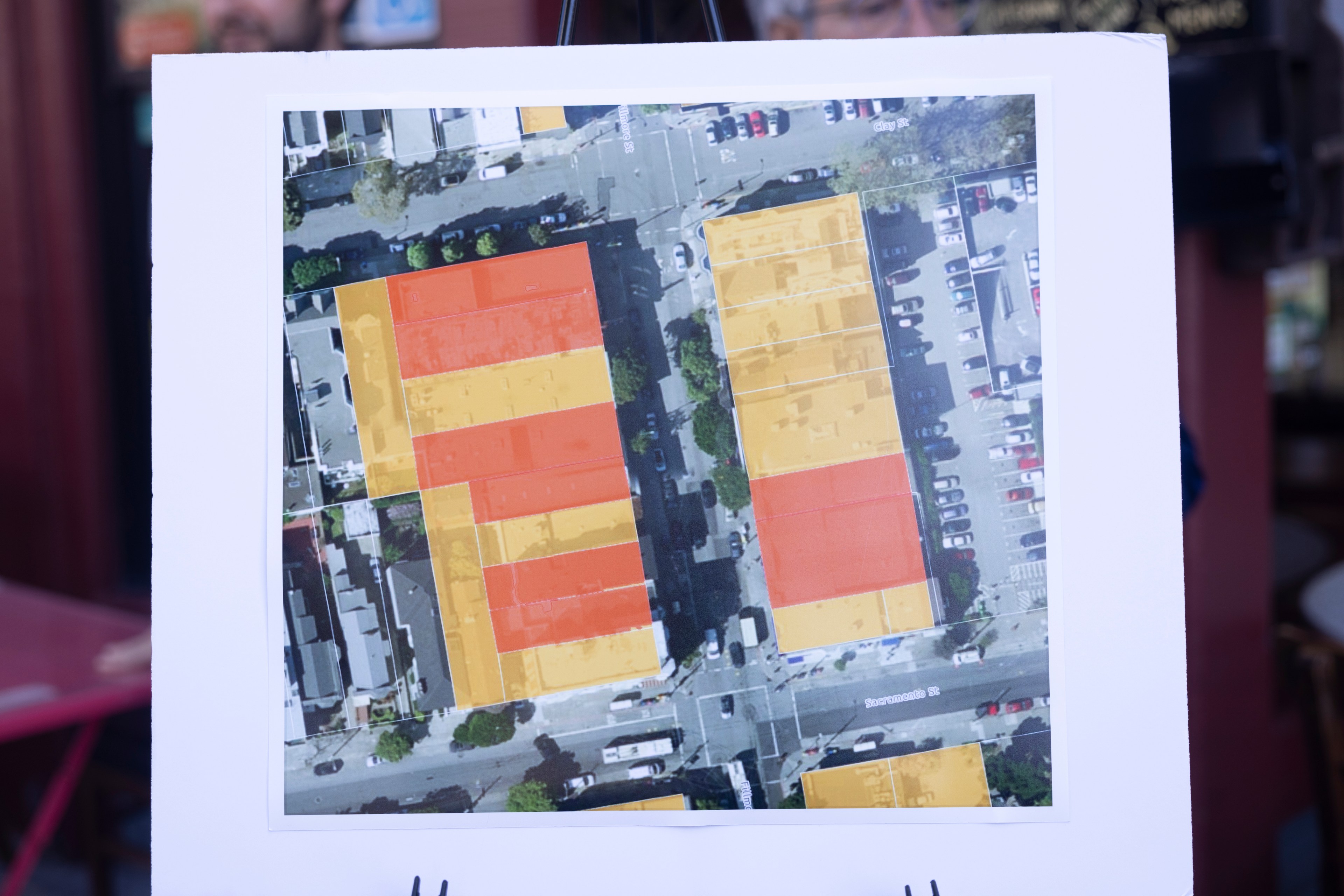 An aerial map depicts a city block highlighted with yellow and red areas, showing buildings and streets with cars parked alongside.