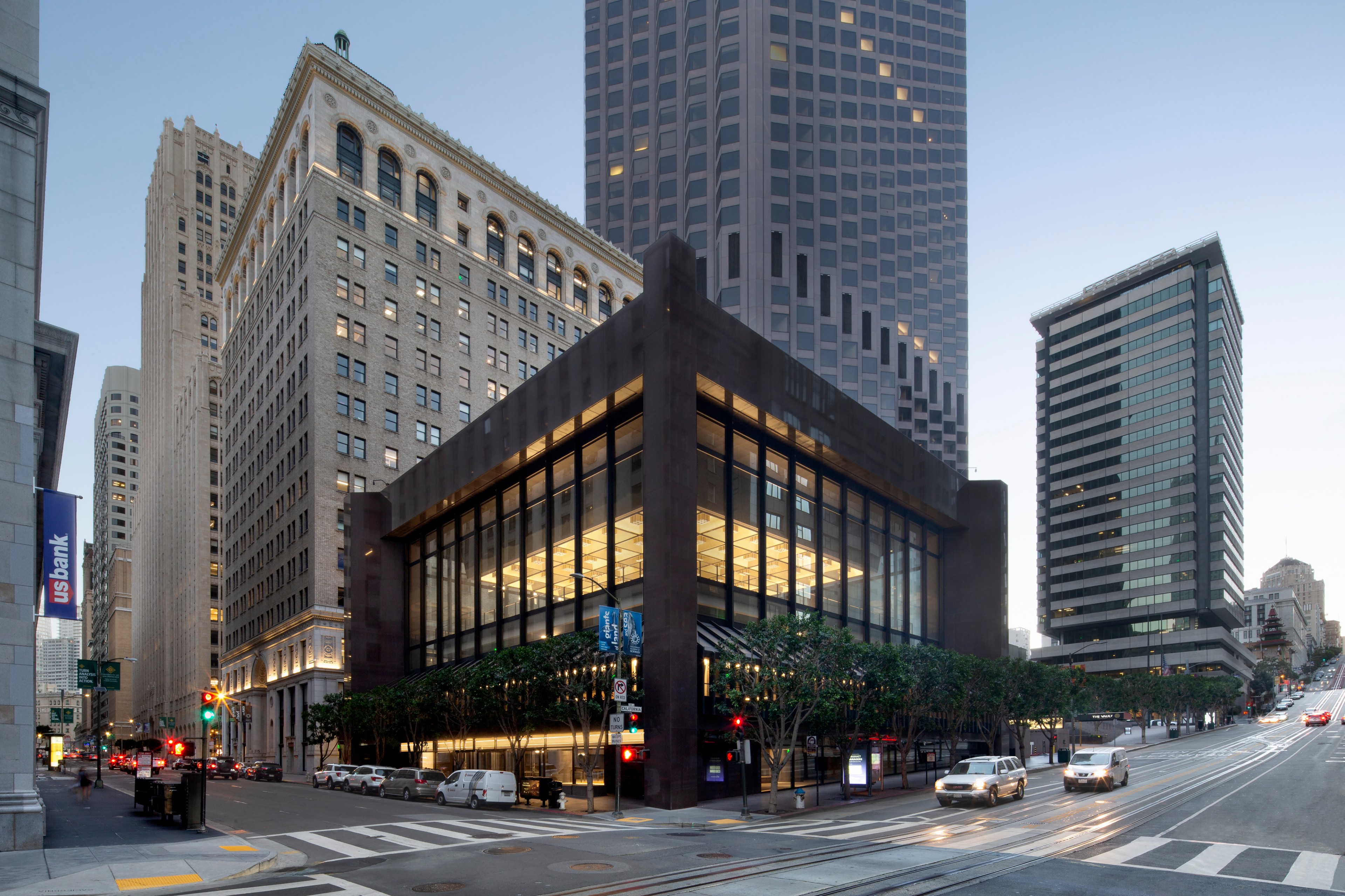 A brown square building sits below many others on a busy downtown corner.