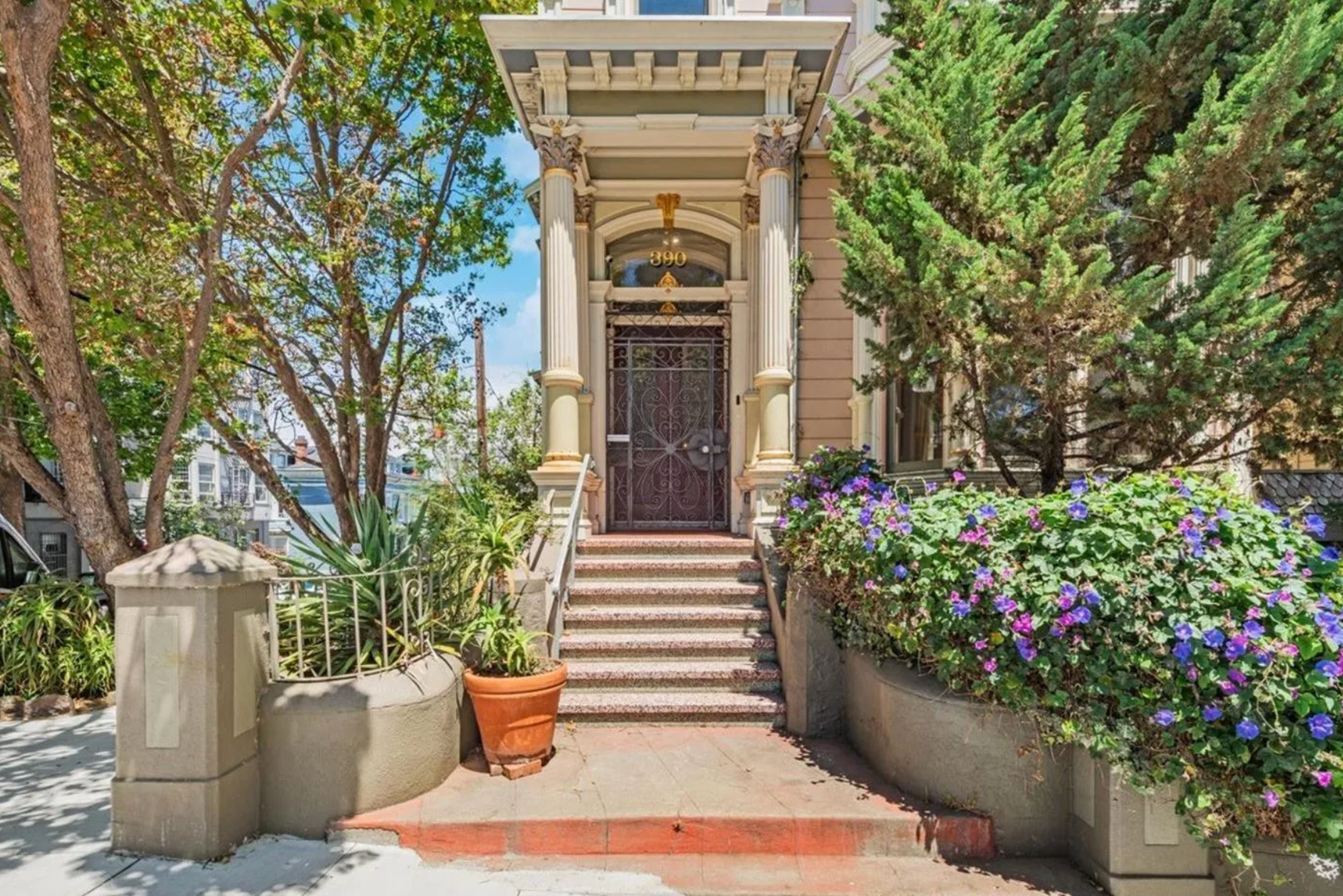 A grand entrance with ornate double doors, flanked by columns, and lush greenery that includes flowers and trees, leading up to a staircase marked &quot;390.&quot;