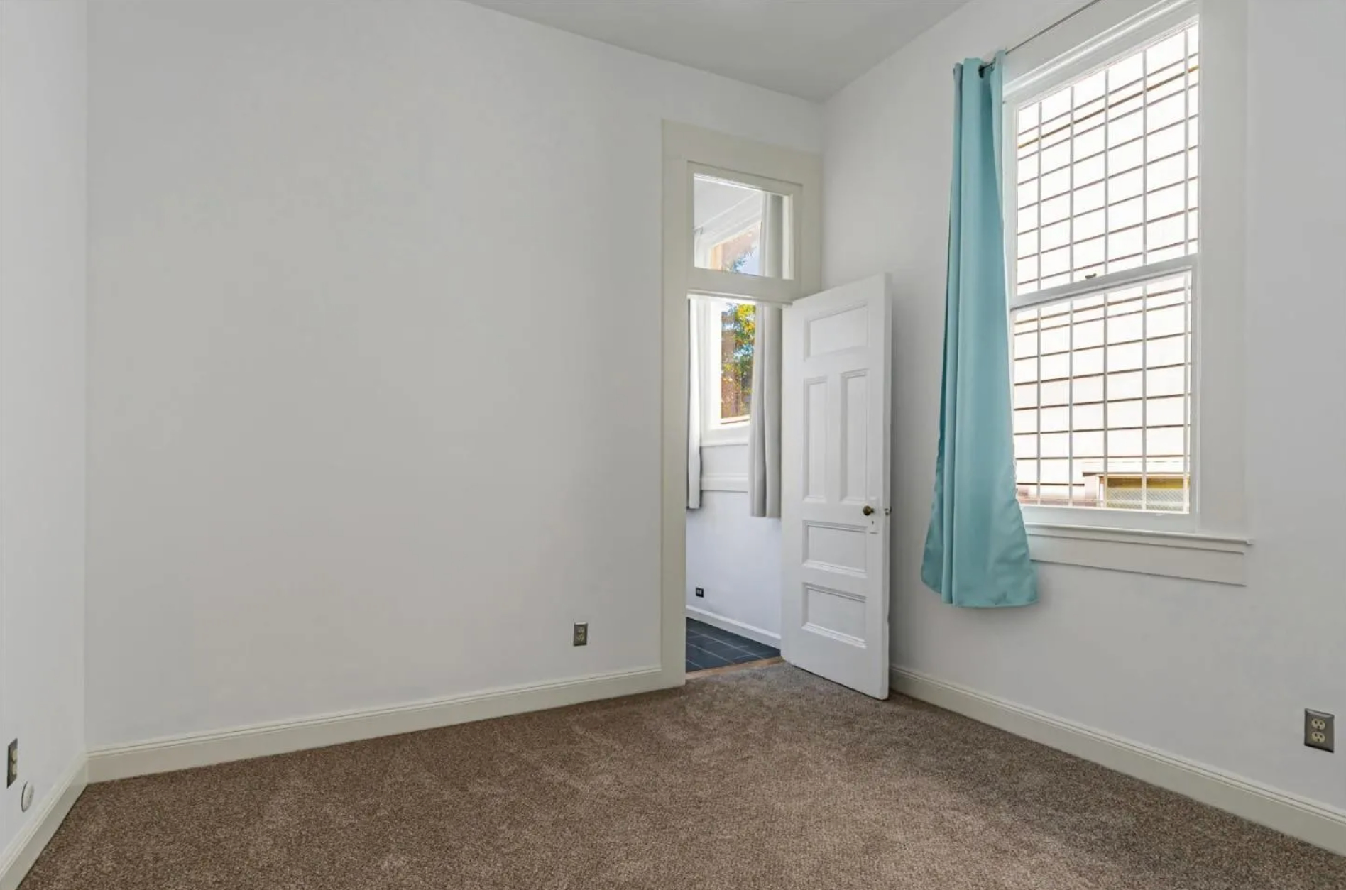 The image shows an empty, carpeted room with white walls, a white door, a window with white blinds, and light blue curtains. A second window and door are visible.