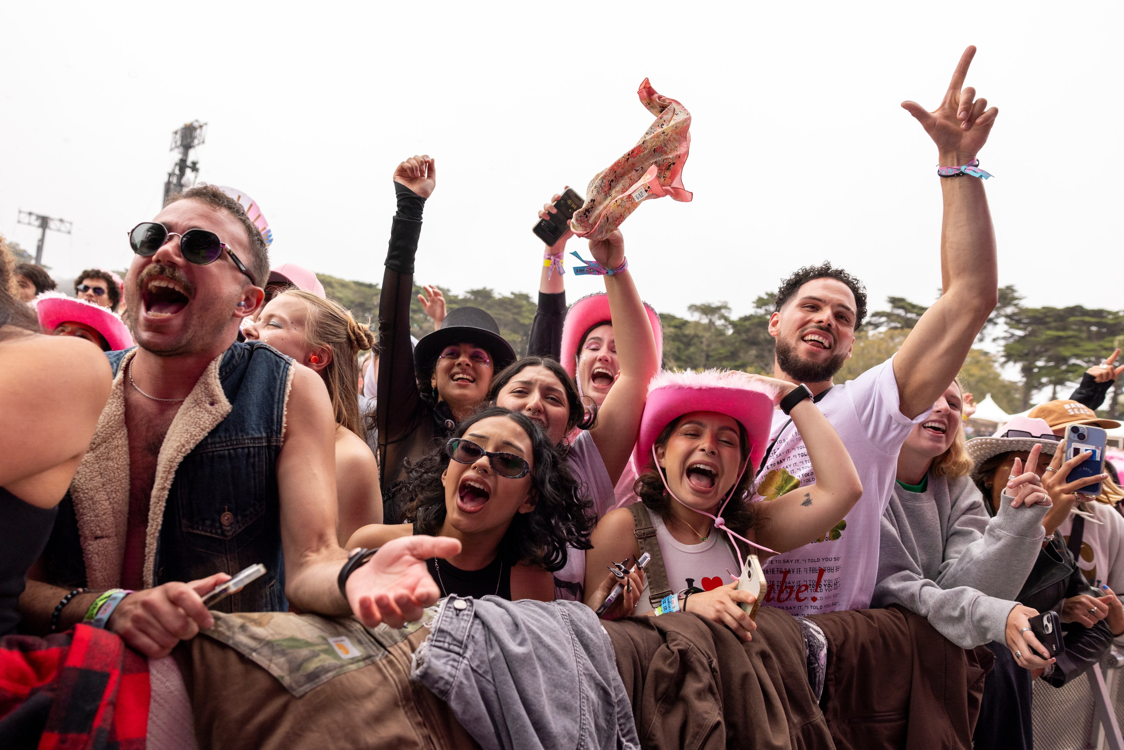 A joyful group of people at a concert, some wearing pink cowboy hats, sunglasses, and excited expressions, cheering and raising their hands enthusiastically.