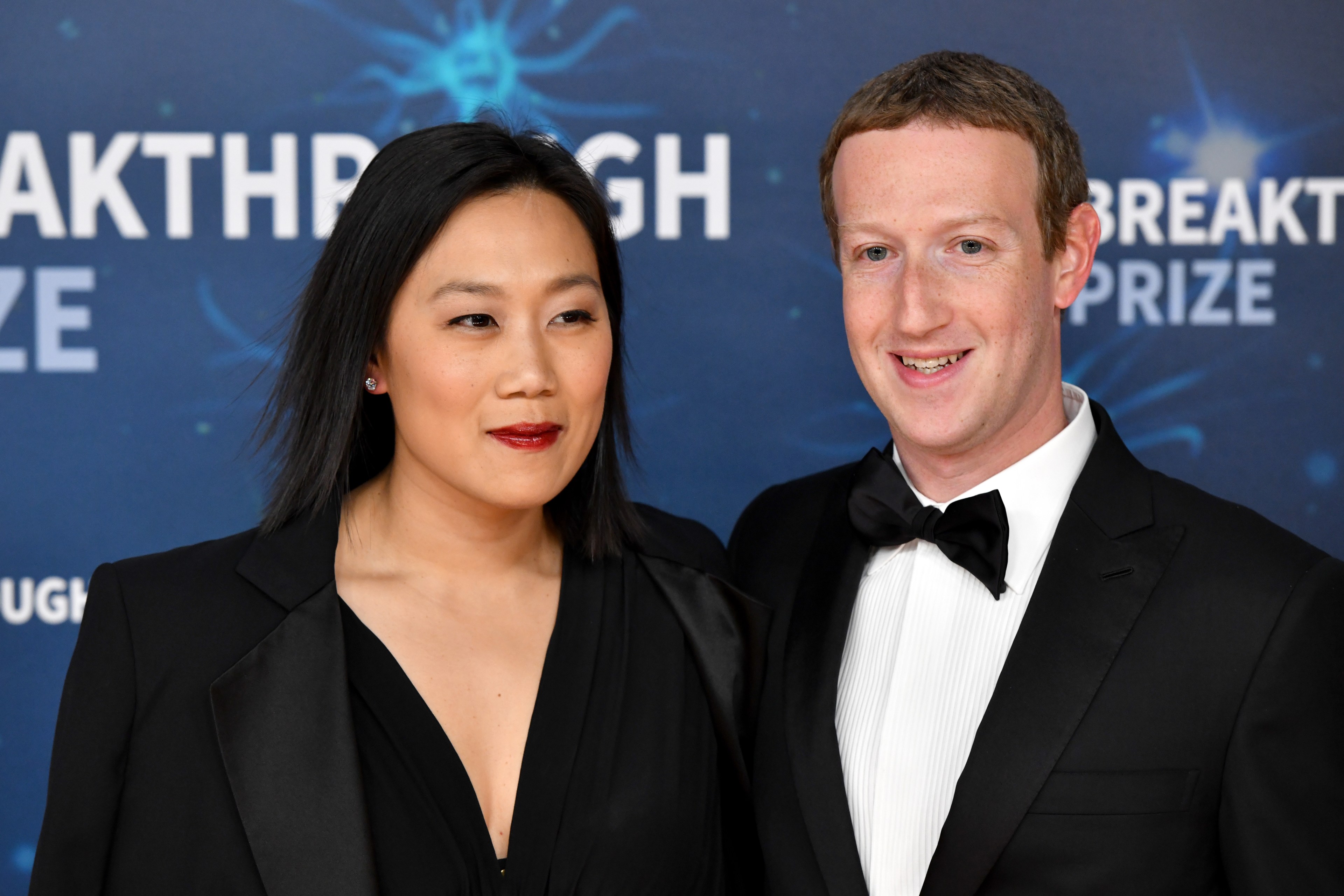 A man and woman are dressed elegantly in formal attire. They stand side by side, smiling in front of a backdrop that says "Breakthrough Prize."