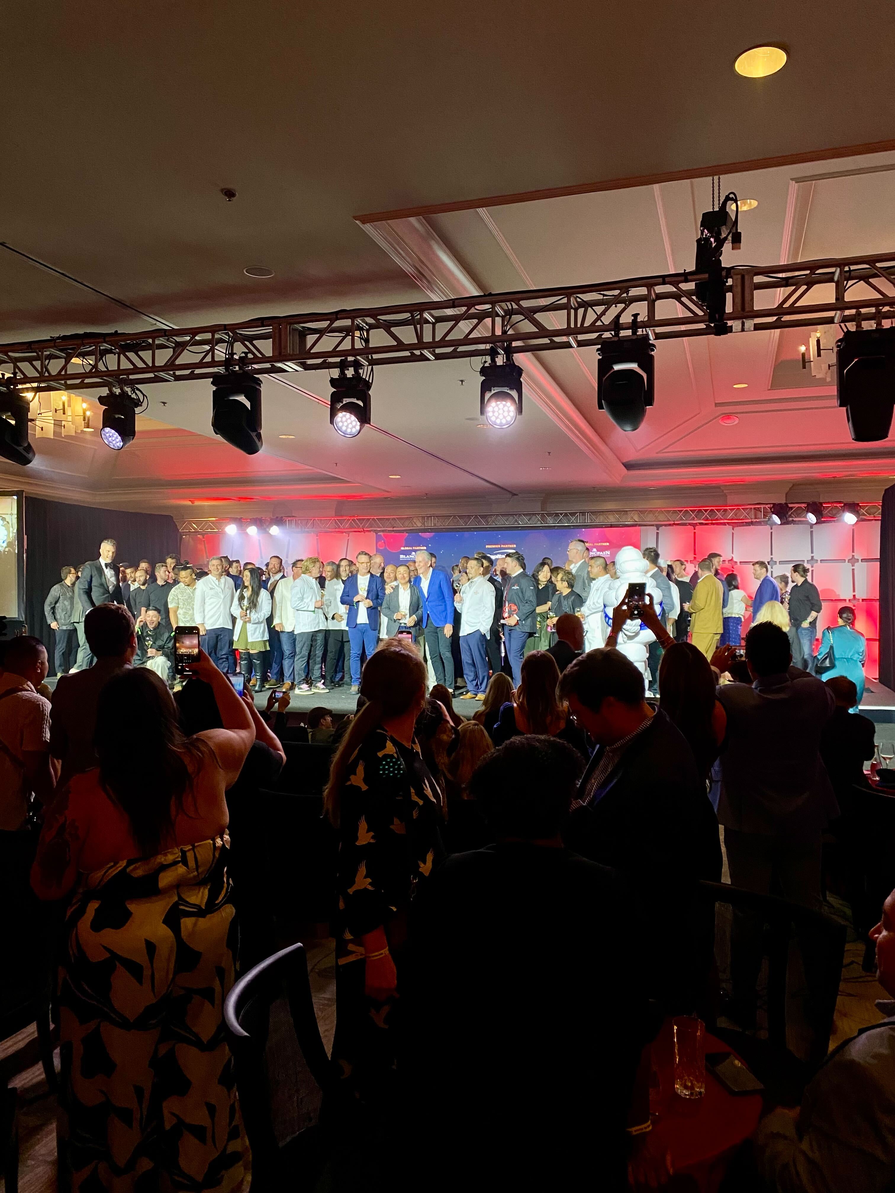 A photo of a large group of chefs on a stage in a hotel banquet room.