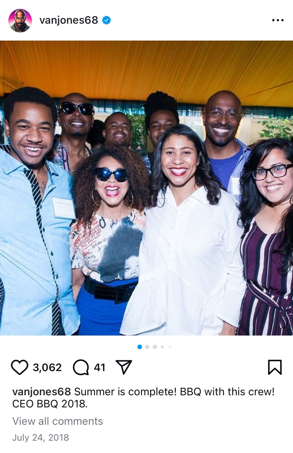 A group of seven people, smiling and standing together, appears in an outdoor setting under a yellow canopy. They seem to be enjoying a summer BBQ event.