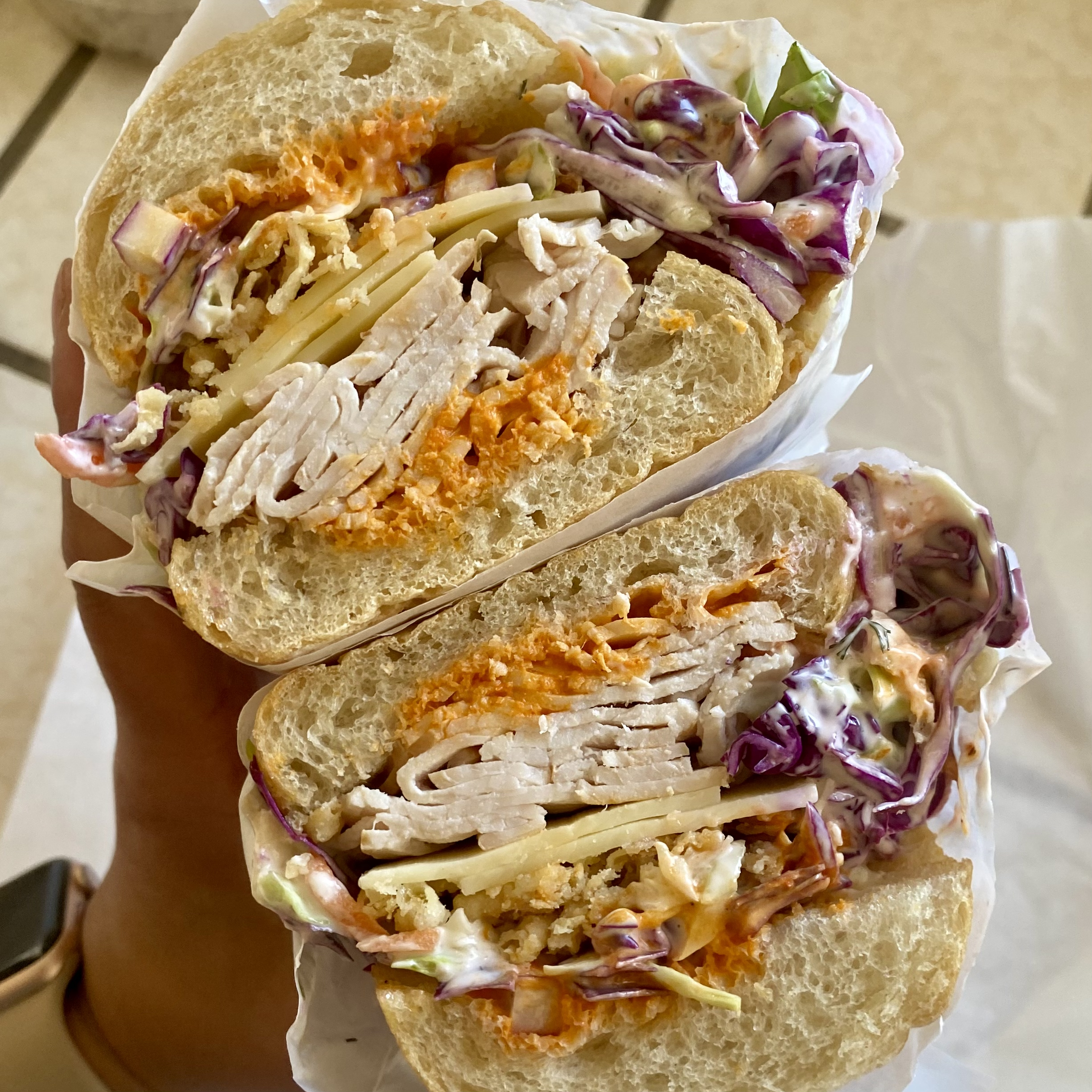 A turkey sandwich cut in half made with sliced cheese and coleslaw.