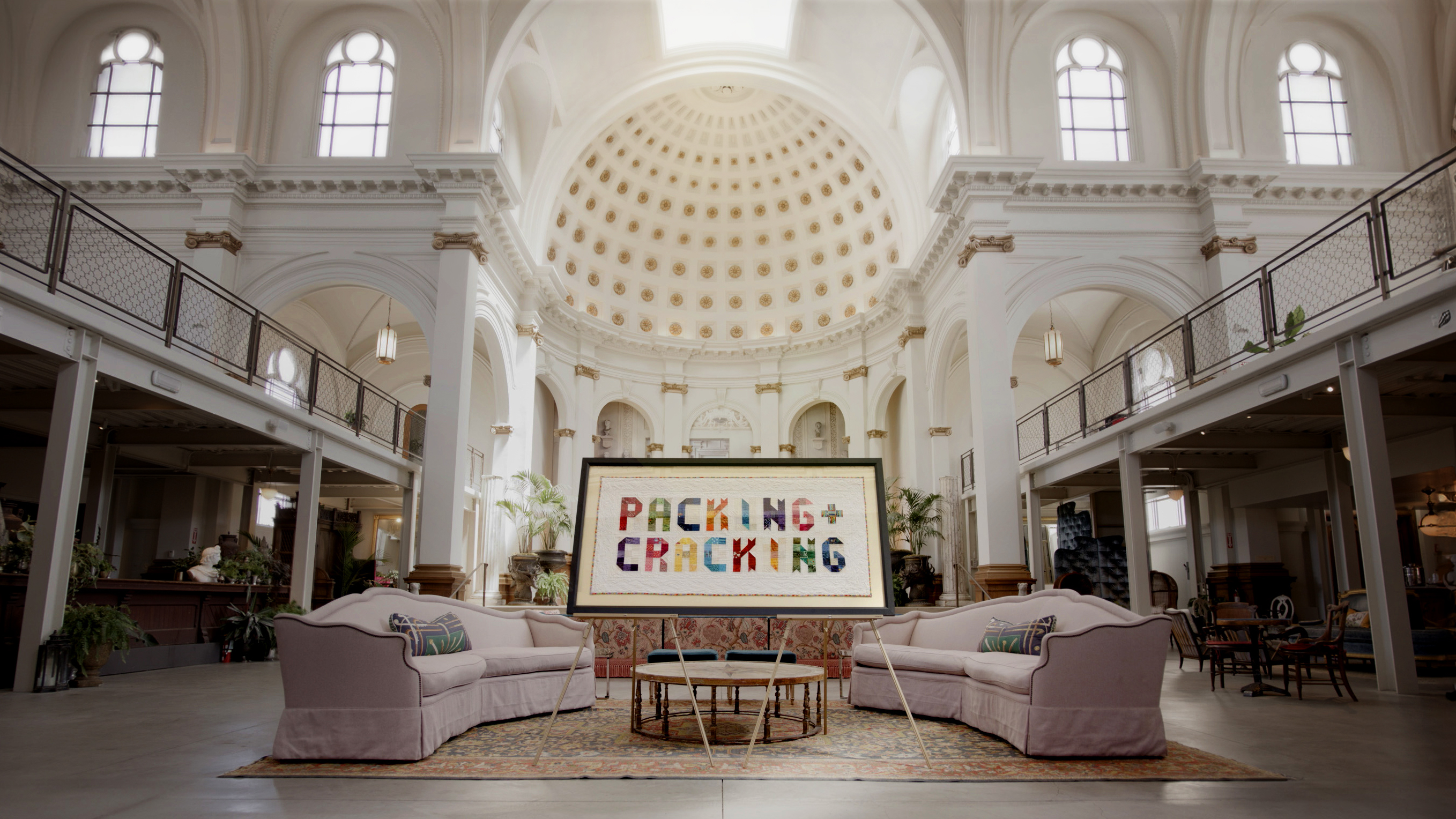 A quilt that reads &quot;Packing + Cracking&quot; sits in a large white church.