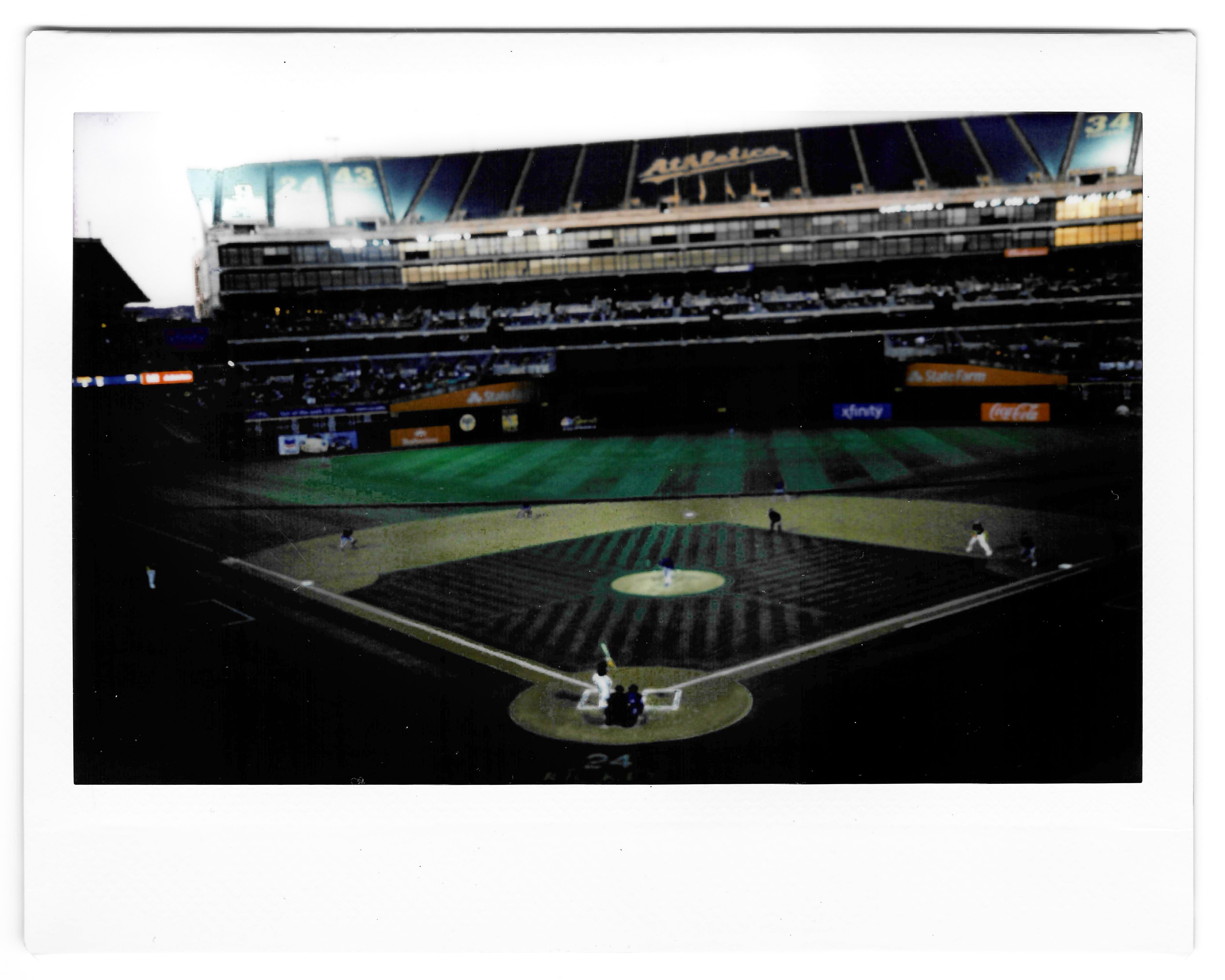 A baseball game is taking place in a large stadium. The pitcher is on the mound mid-throw, and the batter is poised to swing. The field and stands are partially filled.