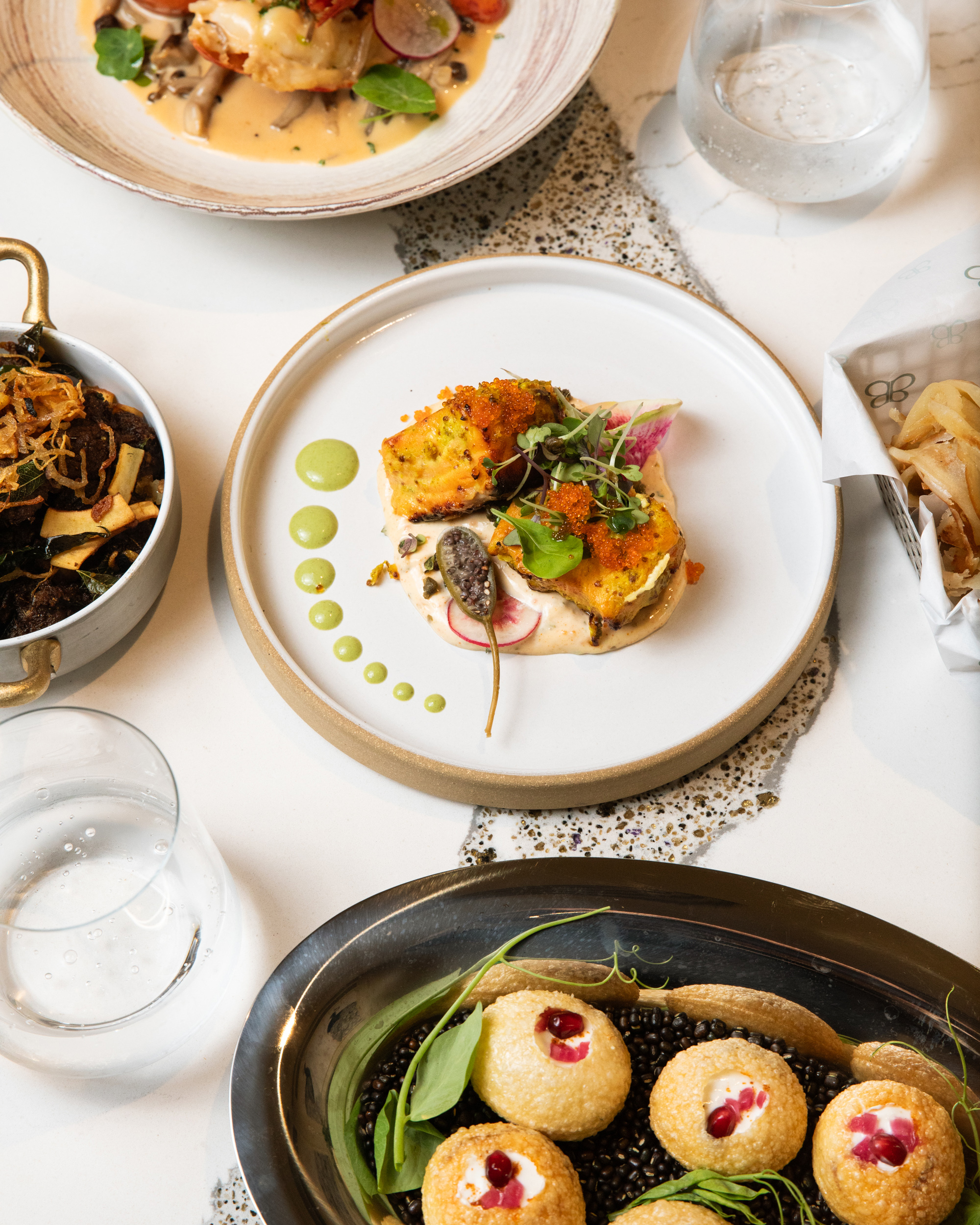 The image showcases an elegant table spread with five gourmet dishes and a glass of water, highlighting colorful and artfully plated food.