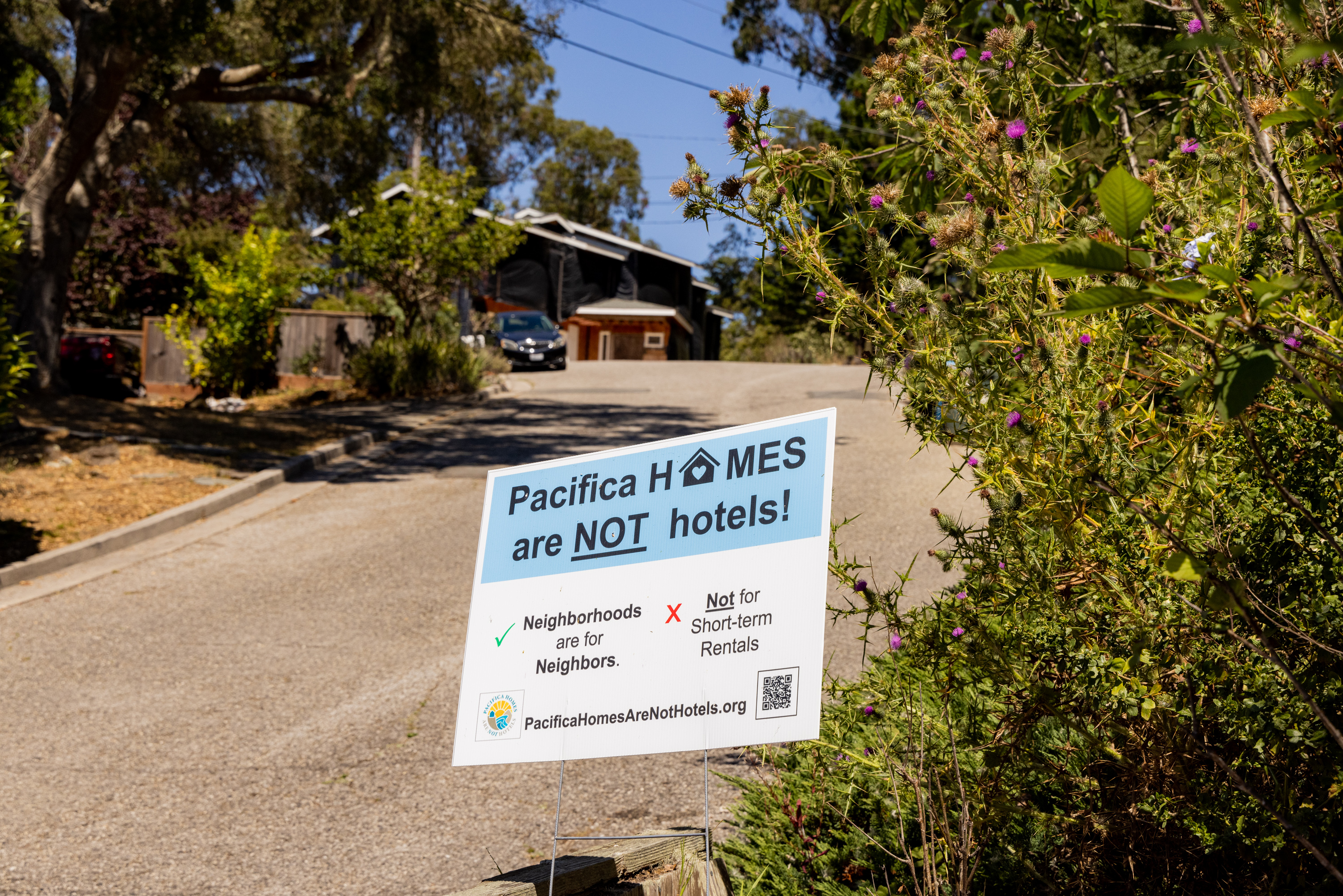 The image shows a sign on a neighborhood street that reads, “Pacifica HOMES are NOT hotels! Neighborhoods are for Neighbors. Not for Short-term Rentals.”