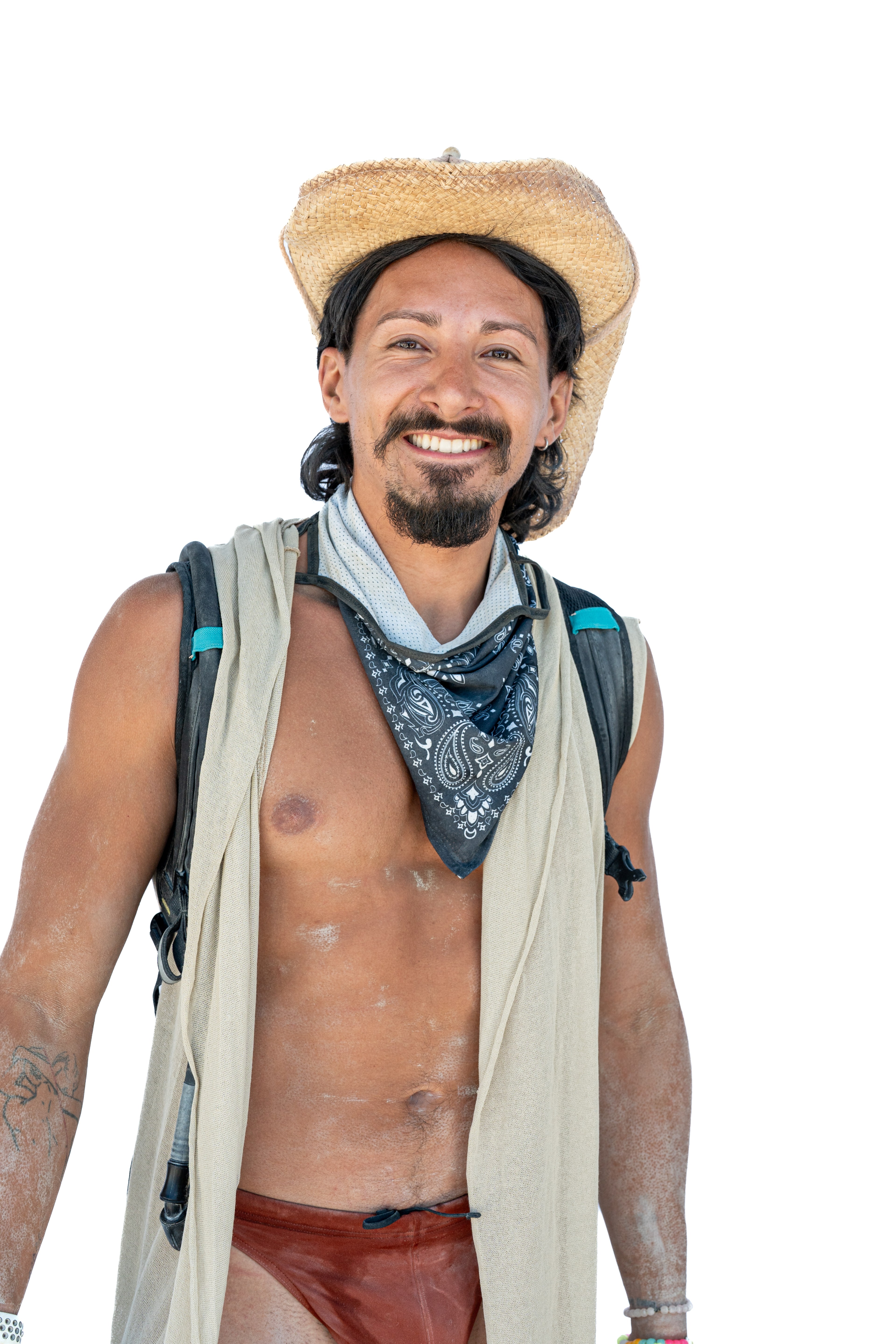 The image shows a smiling man wearing a straw hat, a blue bandana, and a light-colored vest. He's shirtless with a red loincloth and has a backpack on.