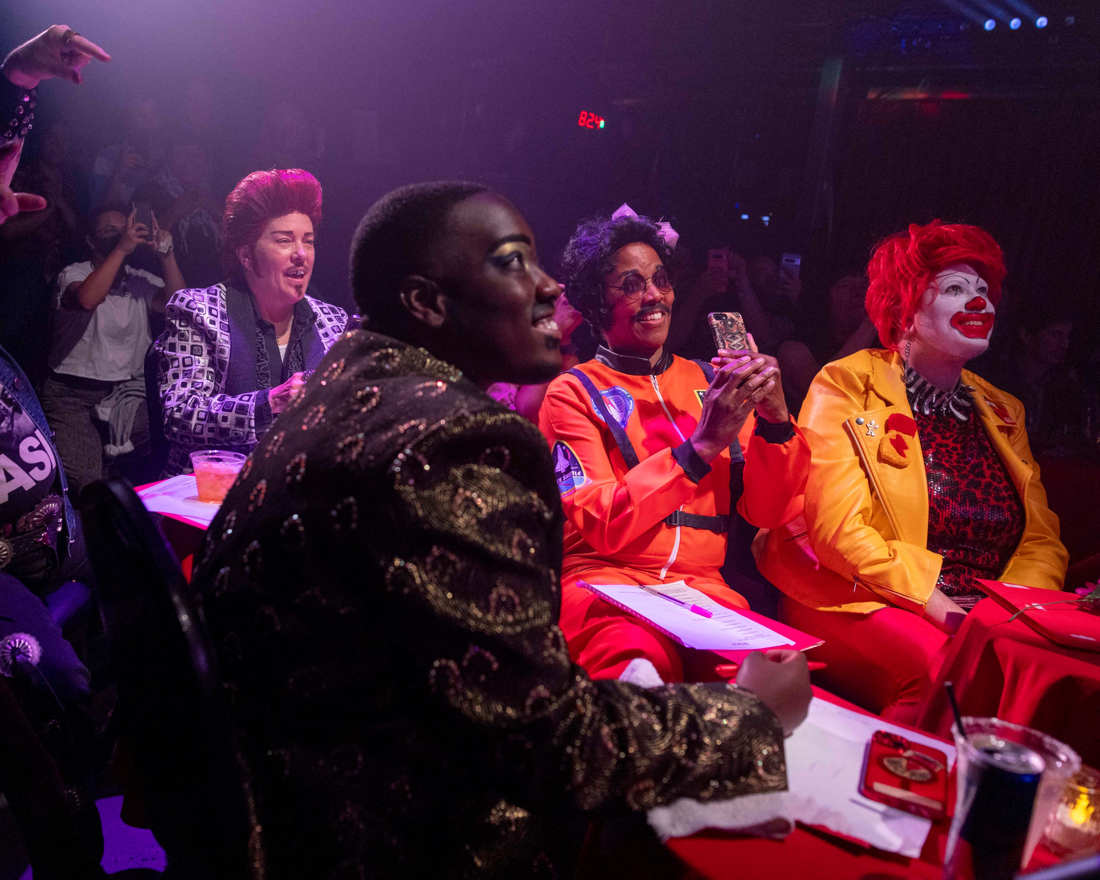 Judges in fancy dress watch a show, one looks like Ronald McDonald.