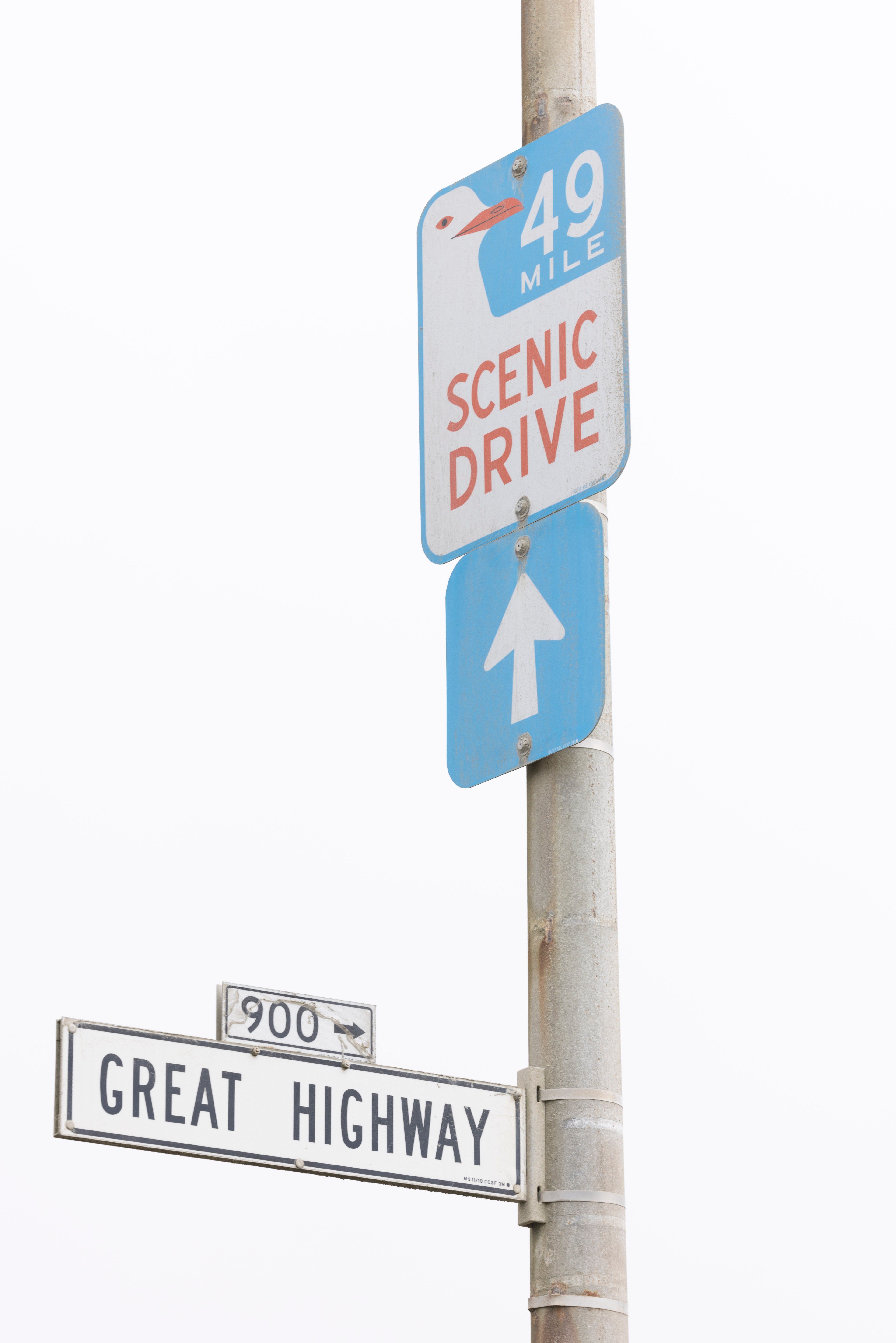 A street sign indicates "49 Mile Scenic Drive" with a blue arrow, while a white sign below labels the location as "Great Highway 900."