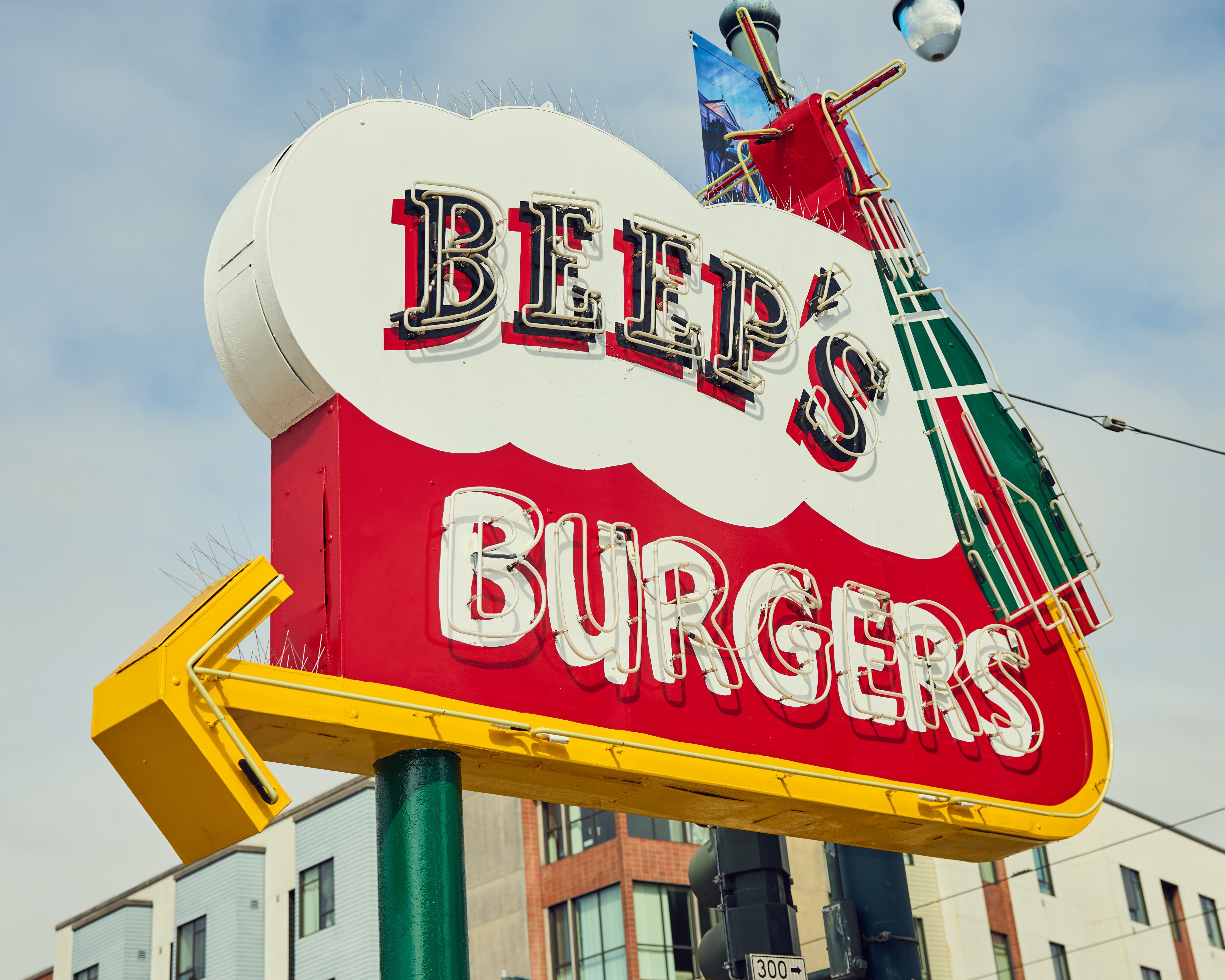The image shows a retro-style sign for &quot;Beep's Burgers&quot; with neon letters on a red and white background, featuring a yellow arrow pointing left.