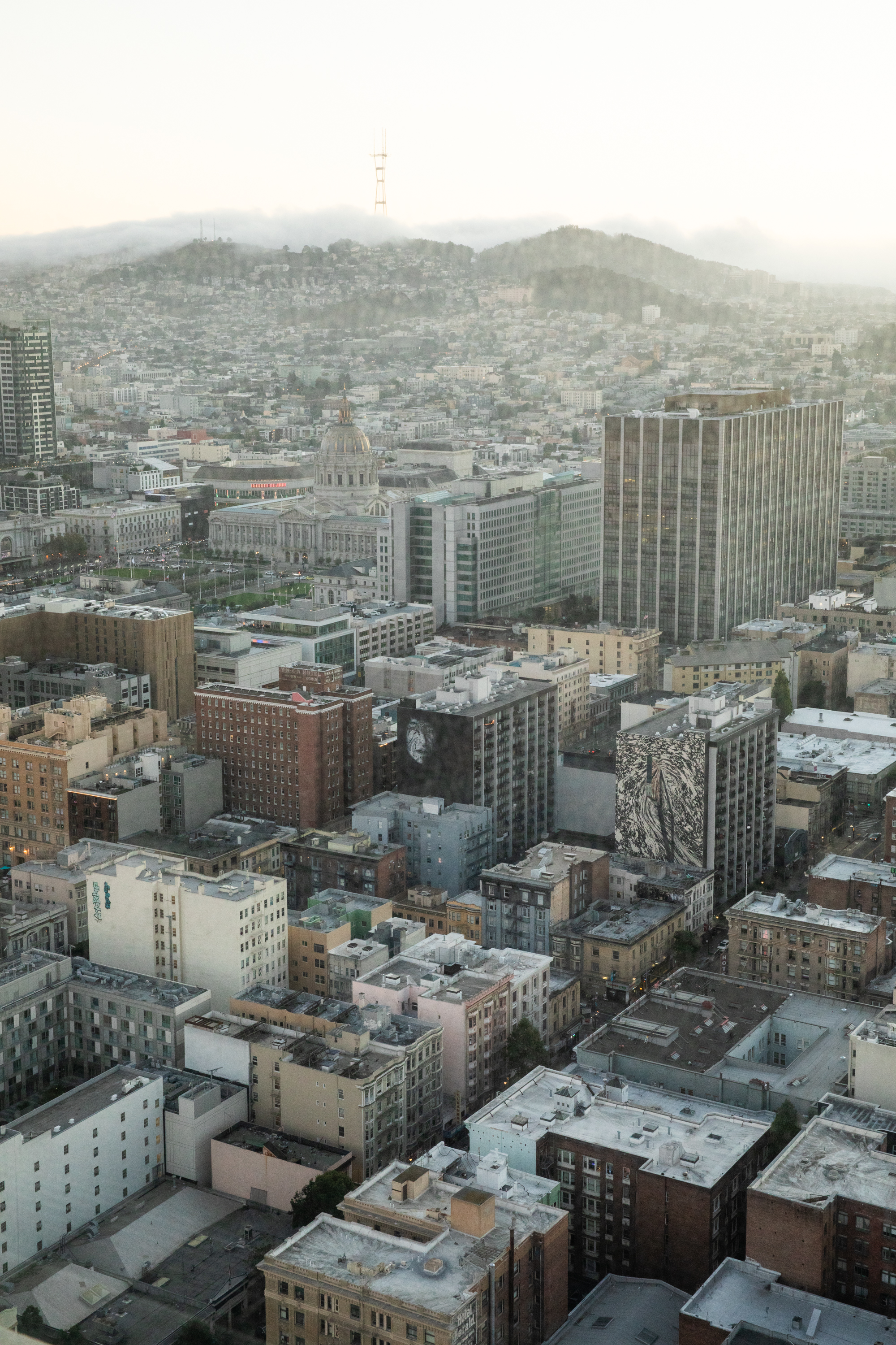 The image shows a cityscape with numerous buildings, including a prominent domed structure and a tall tower on a distant, fog-covered hill. The scene is viewed from above.