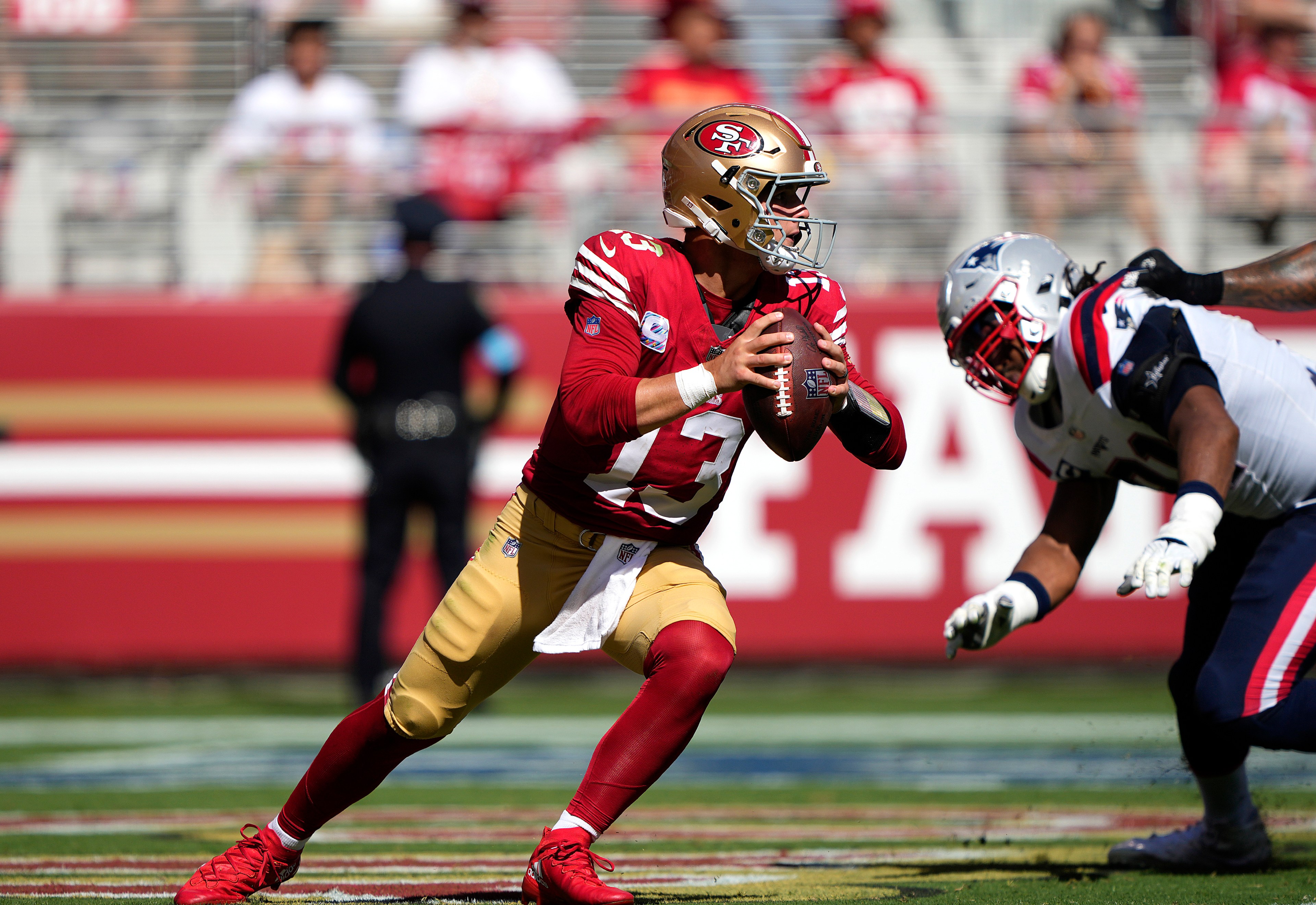 A football player in a red and gold uniform is holding a ball, preparing to make a move. A player in a white and navy uniform is approaching to tackle him.