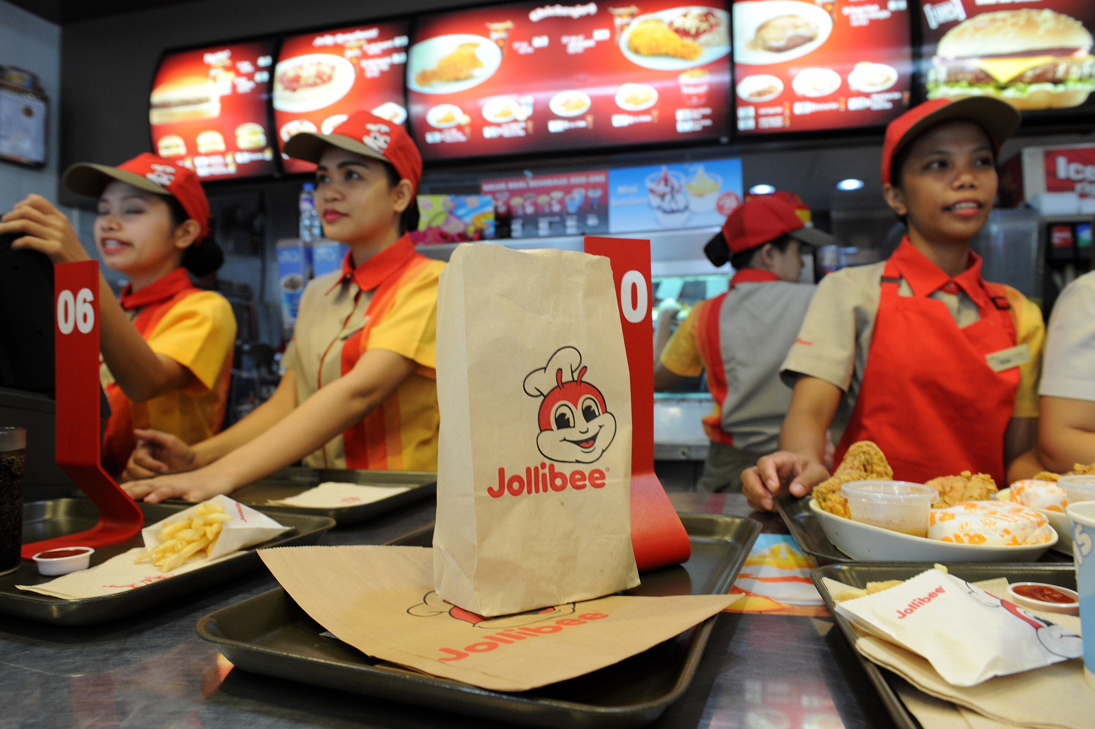 A paper bag with the Jollibee logo sits on a tray on a counter in a fast food restaurant.