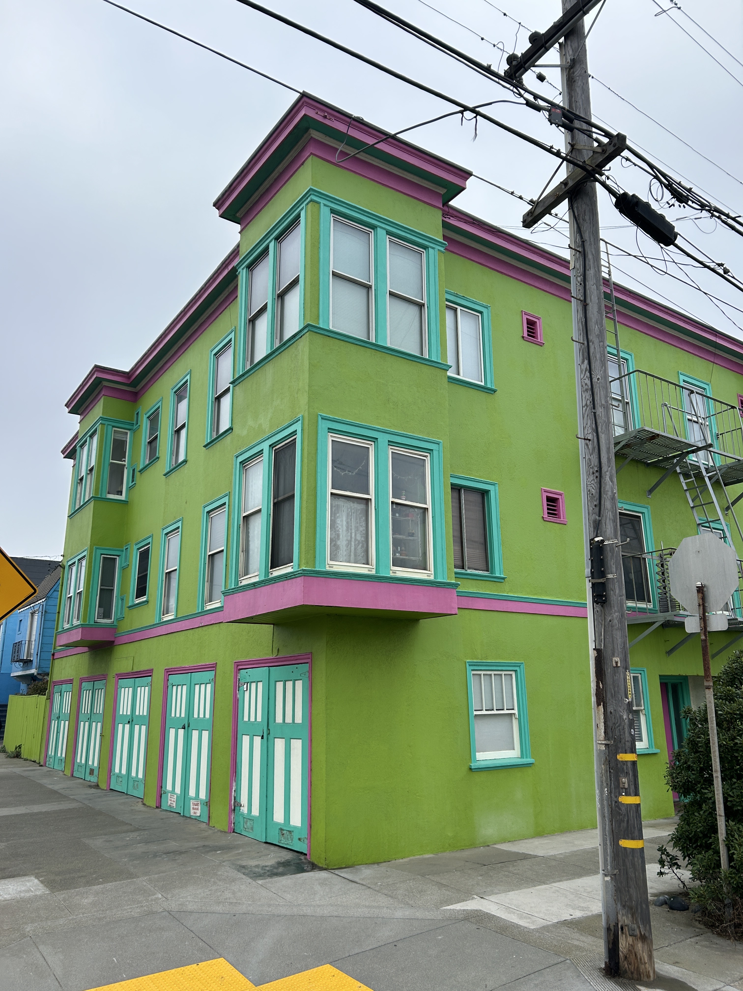 This image shows a lime green corner building with teal and pink trim, multiple windows, and garage doors. There's a utility pole and some power lines nearby.