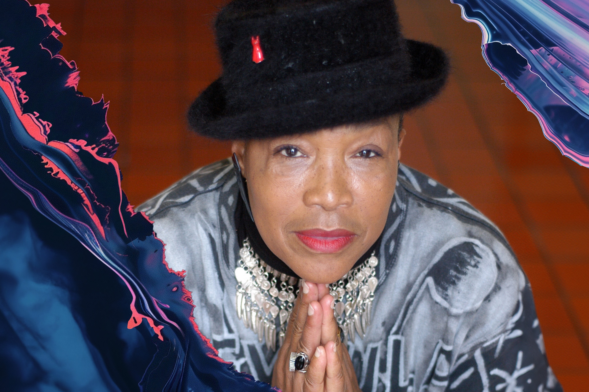 Rhodessa Jones, in a black hat and a patterned shirt, adorned with a large necklace, gazes upward with eyes half-closed, hands pressed together as if in prayer.