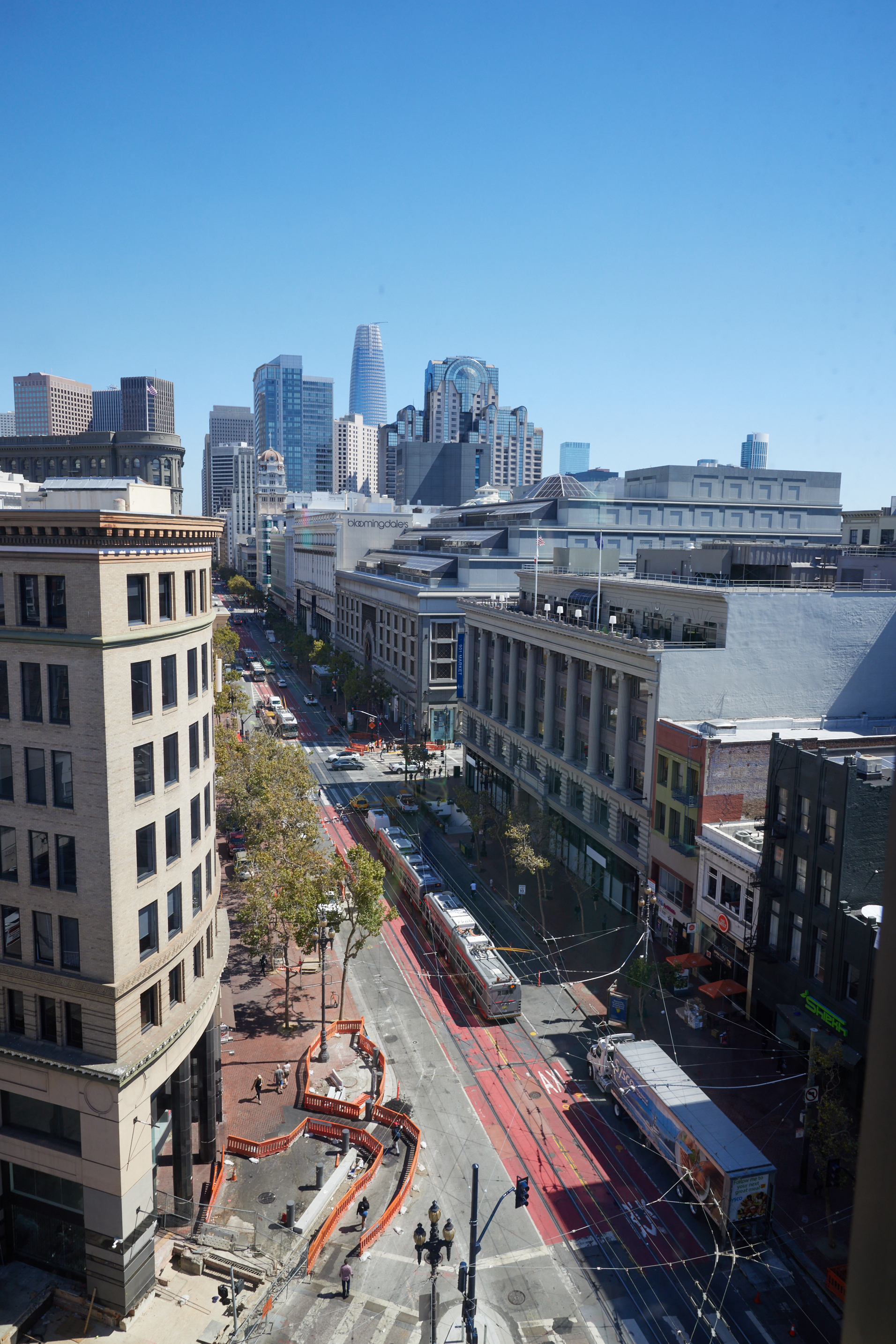 The image depicts an urban street lined with tall buildings and skyscrapers in the background, with a tramway and ongoing road construction visible.