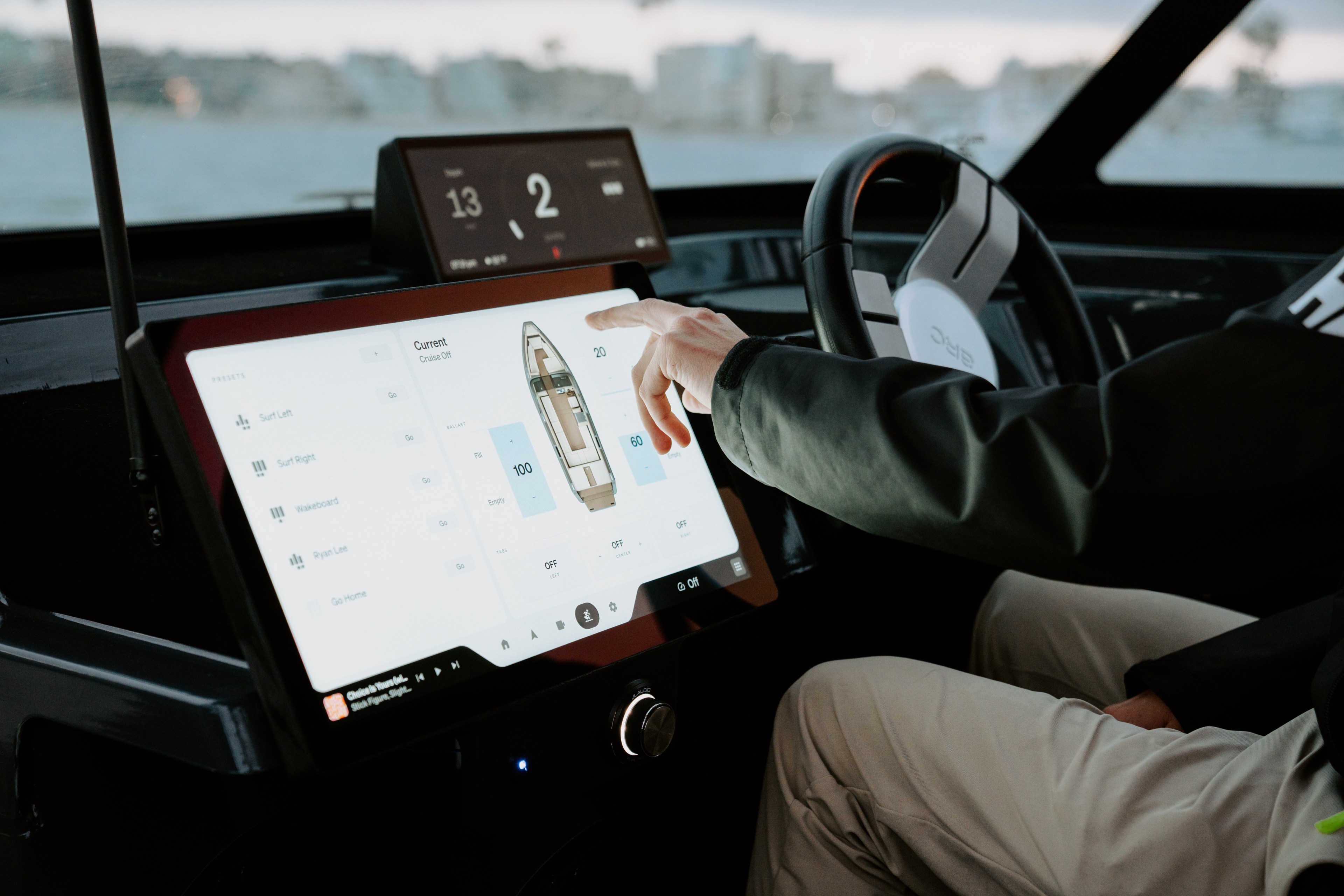 A person is operating a boat using a touchscreen interface. The display shows boat controls and settings, and a hand is interacting with it.