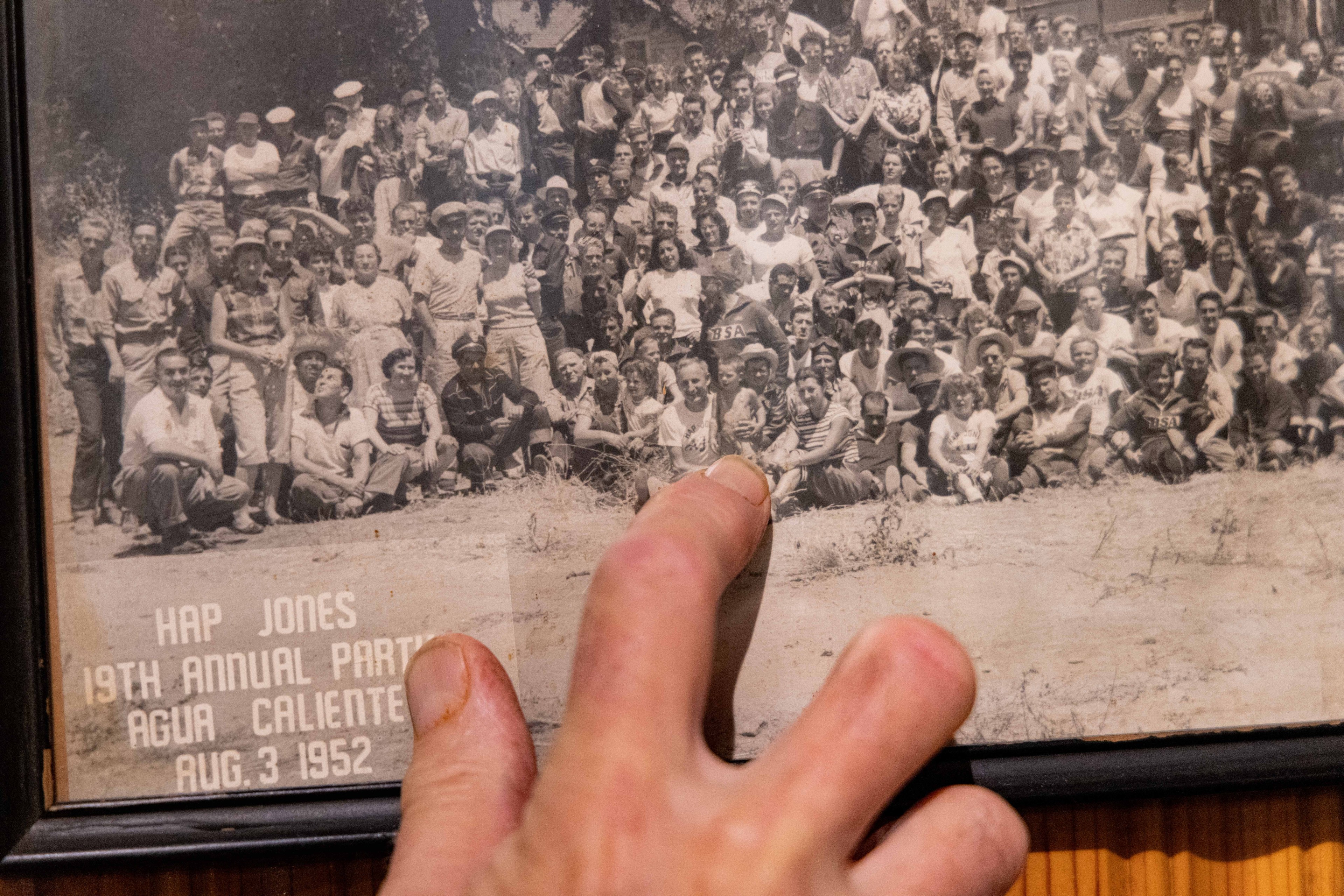 A sepia-toned group photo from August 3, 1952, showing dozens of people at the &quot;Hap Jones 19th Annual Party&quot; in Agua Caliente, with a finger pointing at it.