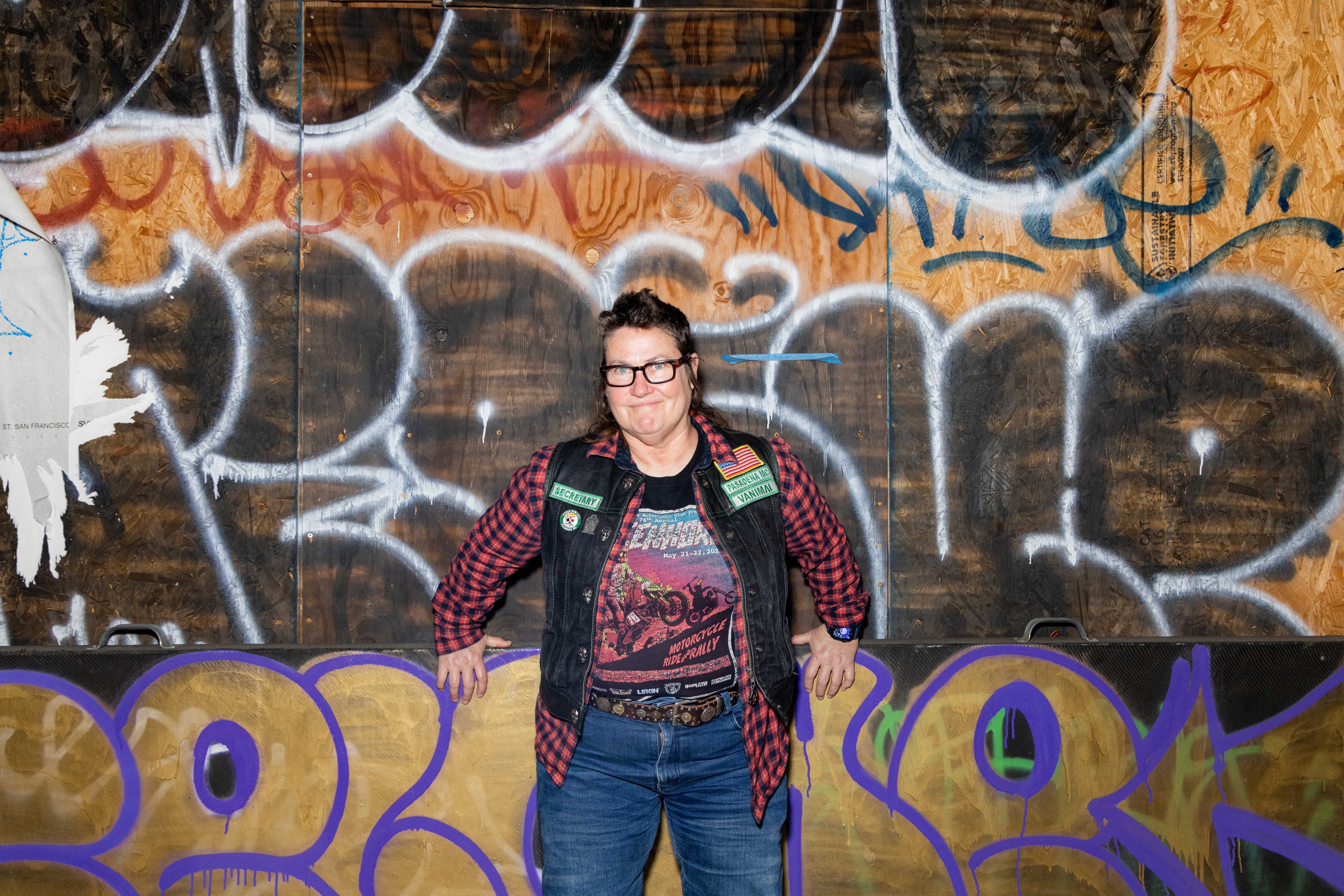 A woman poses in front of a graffiti-covered wall.