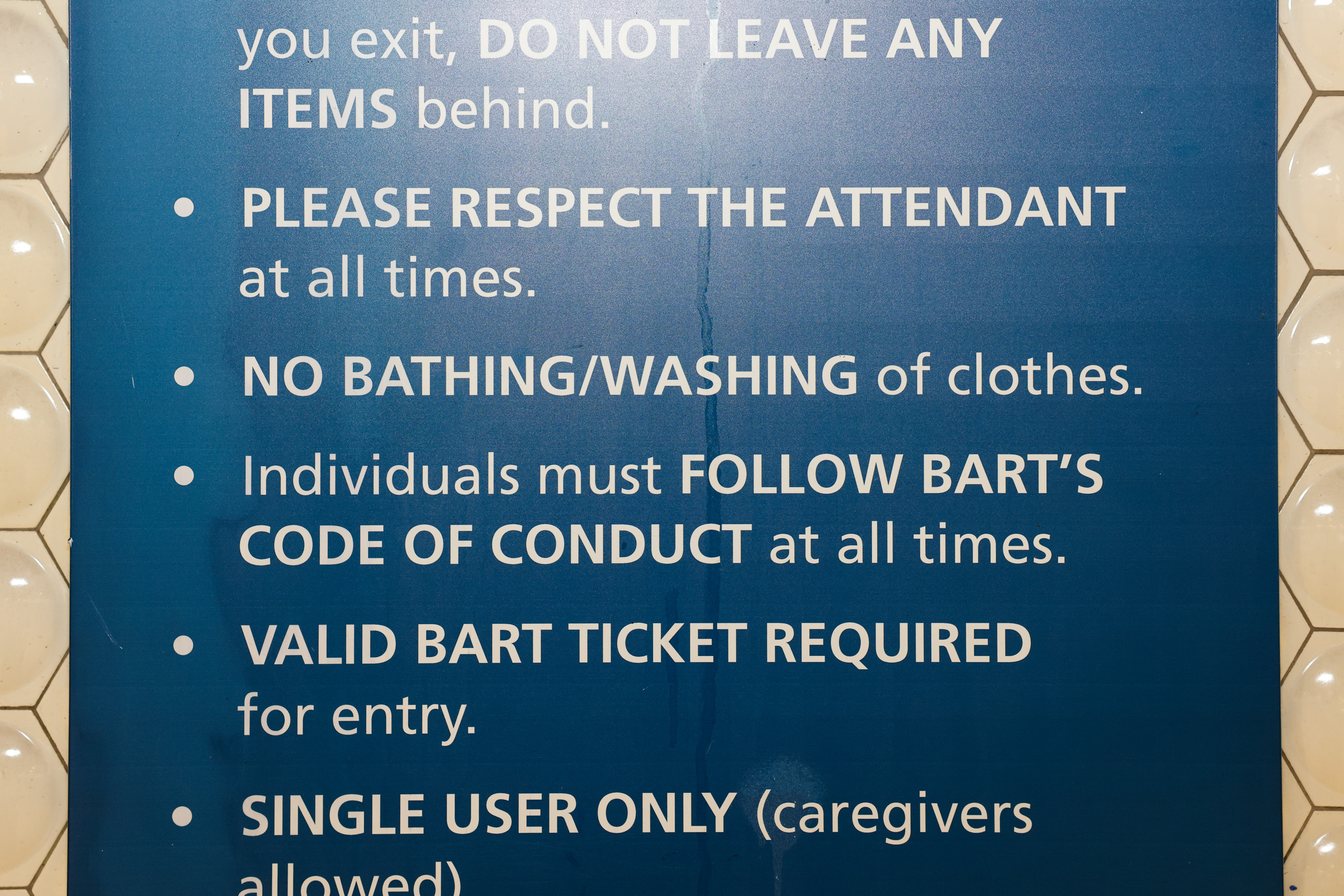 The image shows a blue sign listing BART rules: respect attendants, no bathing, follow conduct codes, require valid tickets, and single user entry.