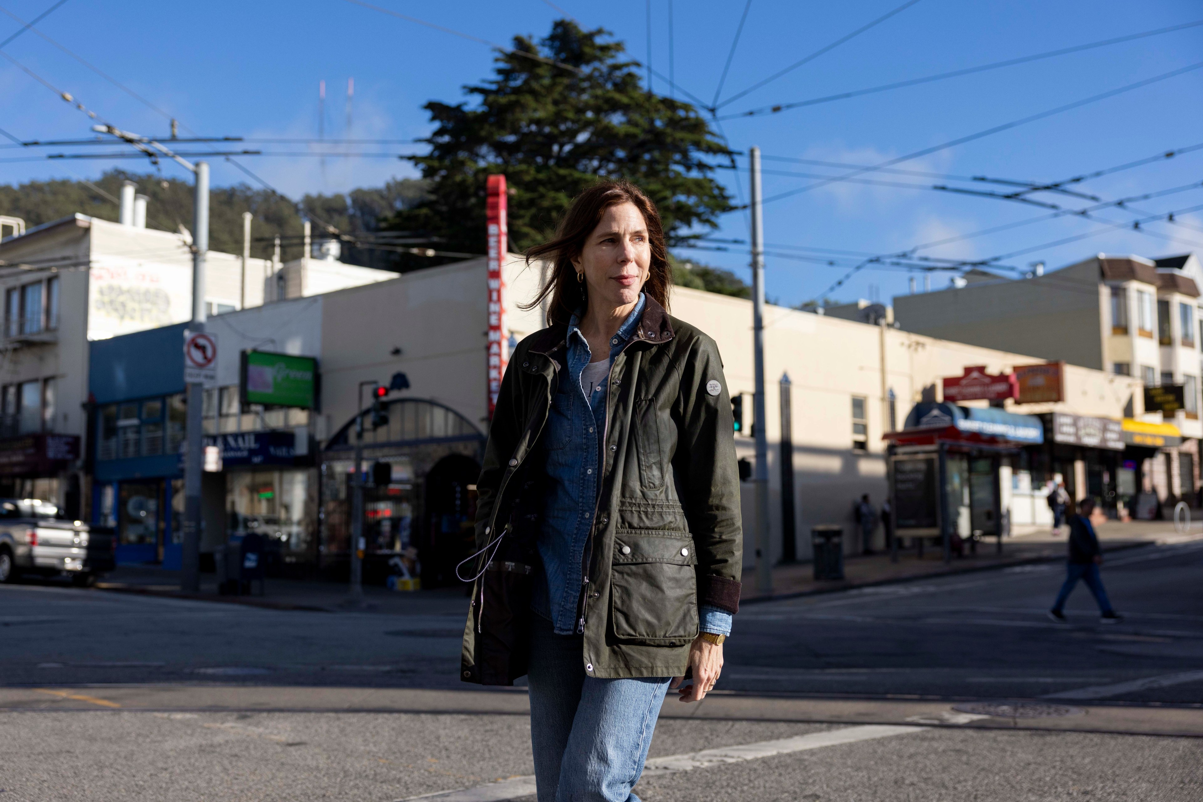 A woman in a green jacket walks across the street.