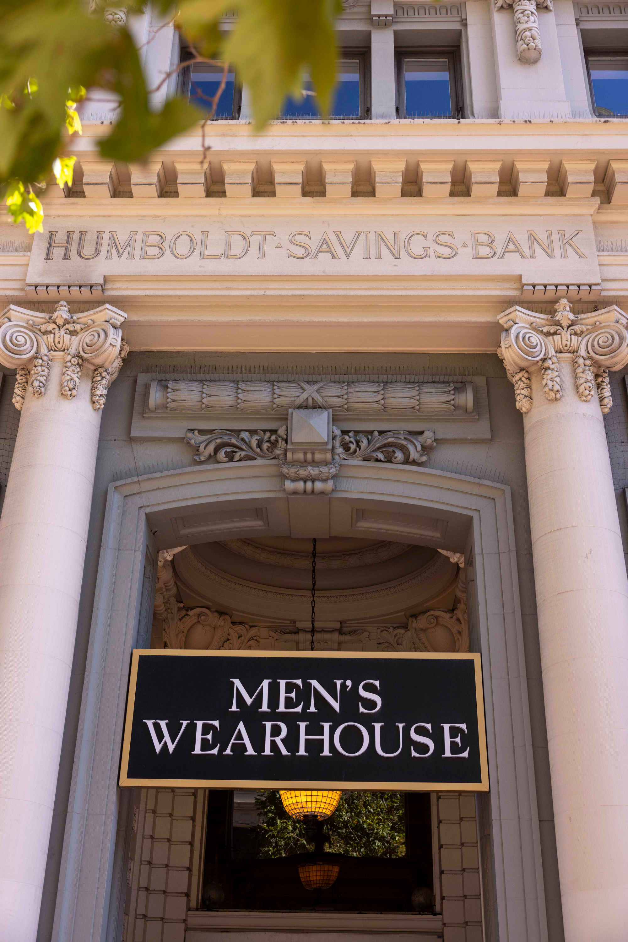 The image shows an ornate building facade with &quot;Humboldt Savings Bank&quot; inscribed above a sign reading &quot;Men's Wearhouse&quot; in white letters on a black background.