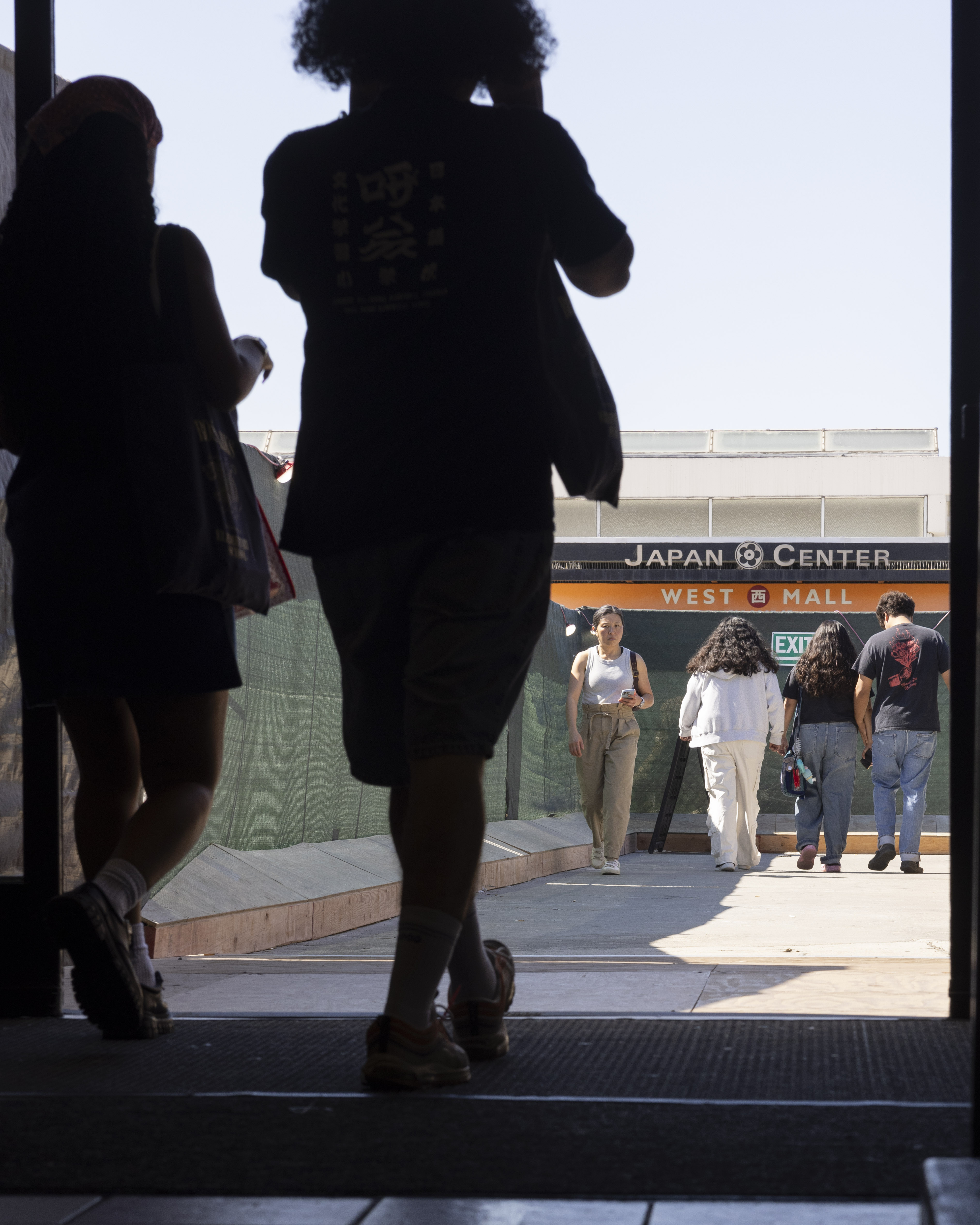 People are walking through a doorway toward the Japan Center West Mall. The scene is backlit, creating silhouettes of the figures against the bright entrance.