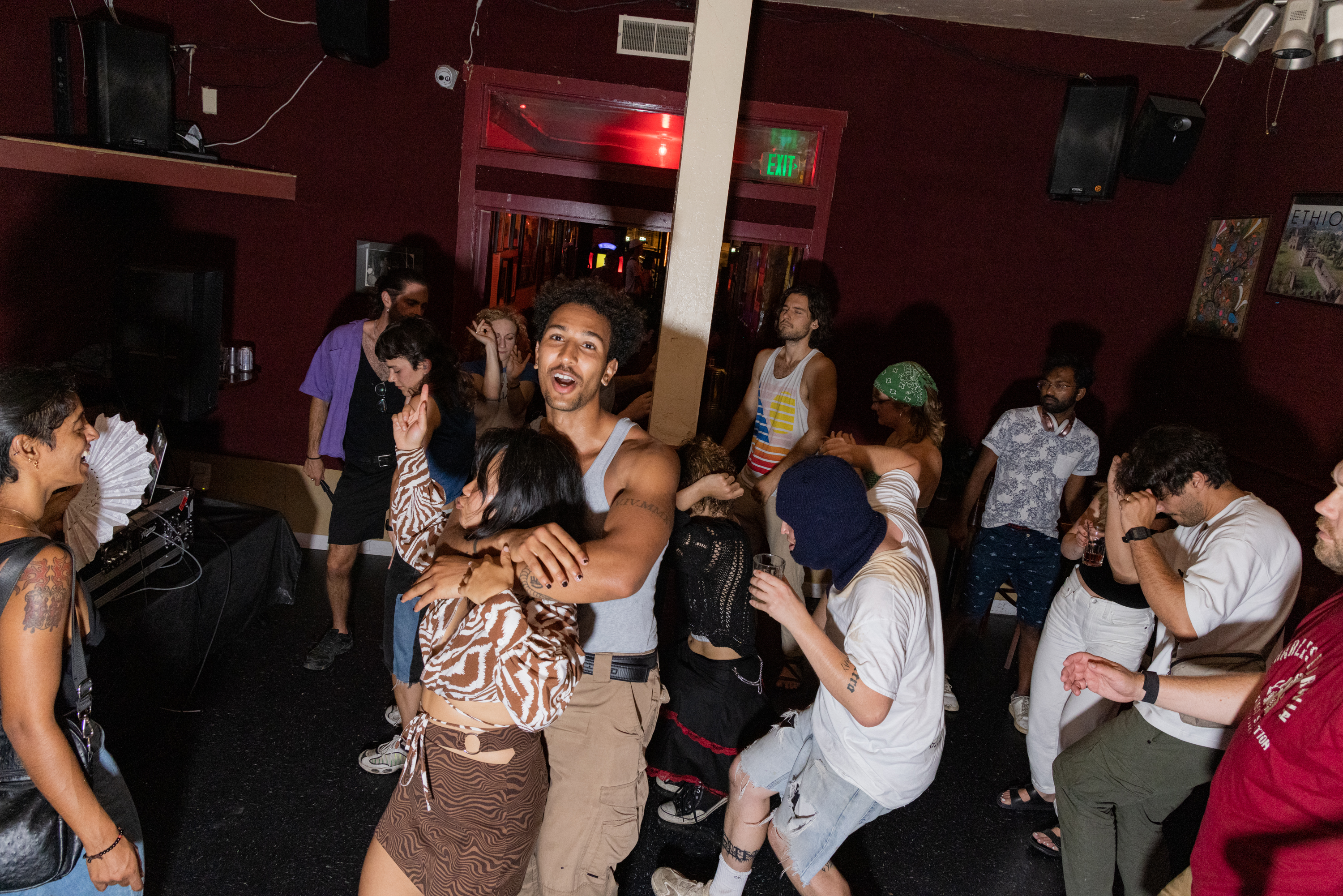 A lively party scene with people dancing energetically in a dimly lit room, featuring various outfits and expressions, creating an upbeat and vibrant atmosphere.