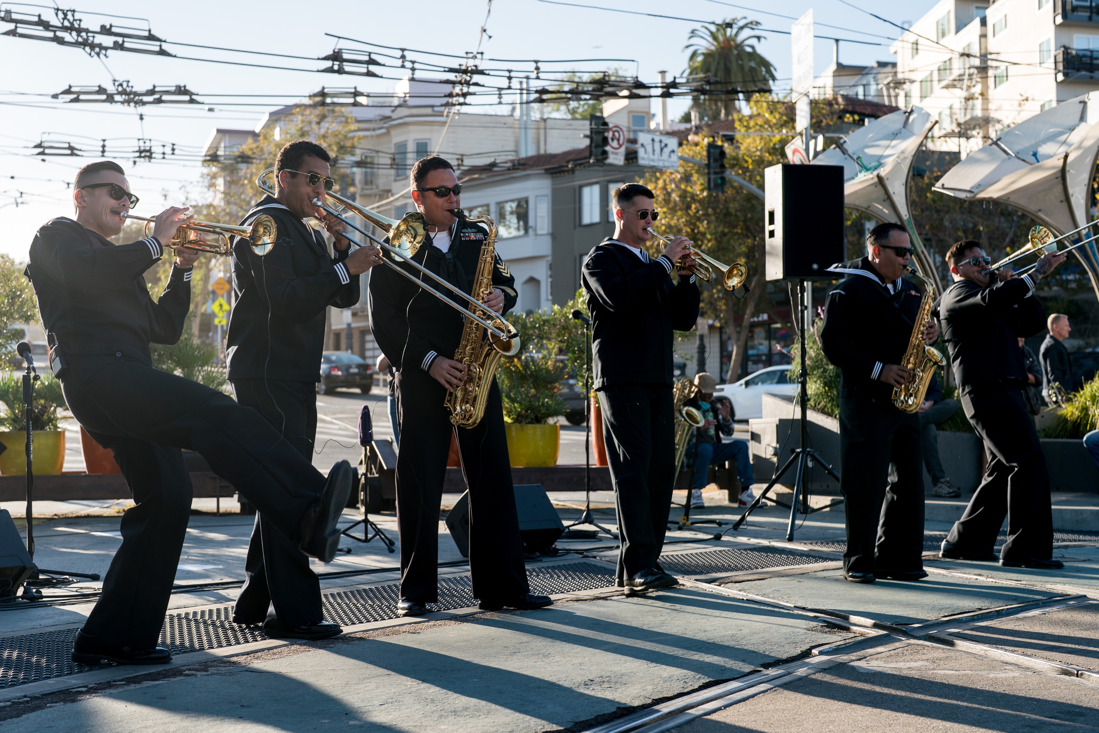 Navy officers play in a brass band on a city sidewalk.