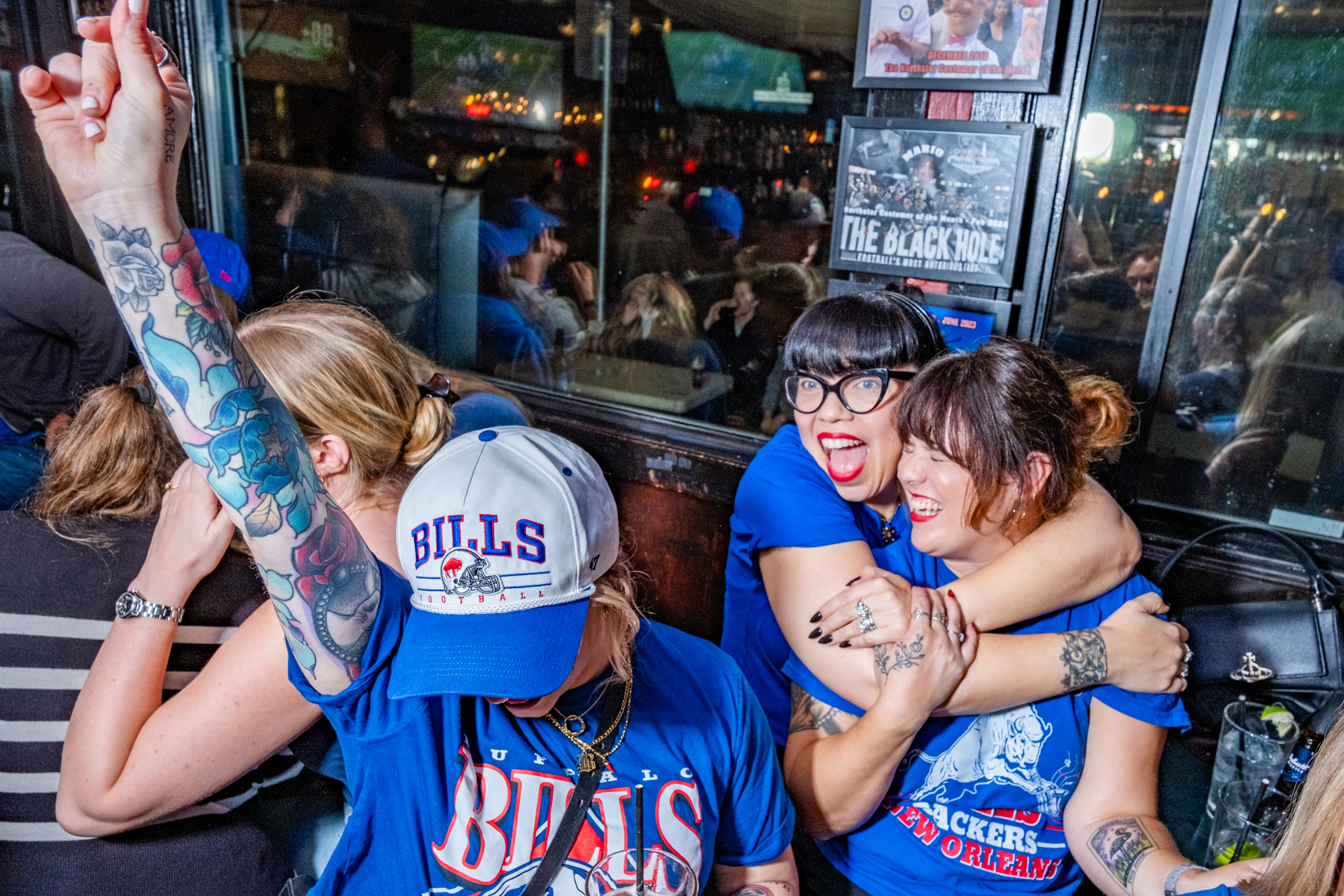 Three women in blue shirts enthusiastically celebrate a Bills game at Northstar cafe.