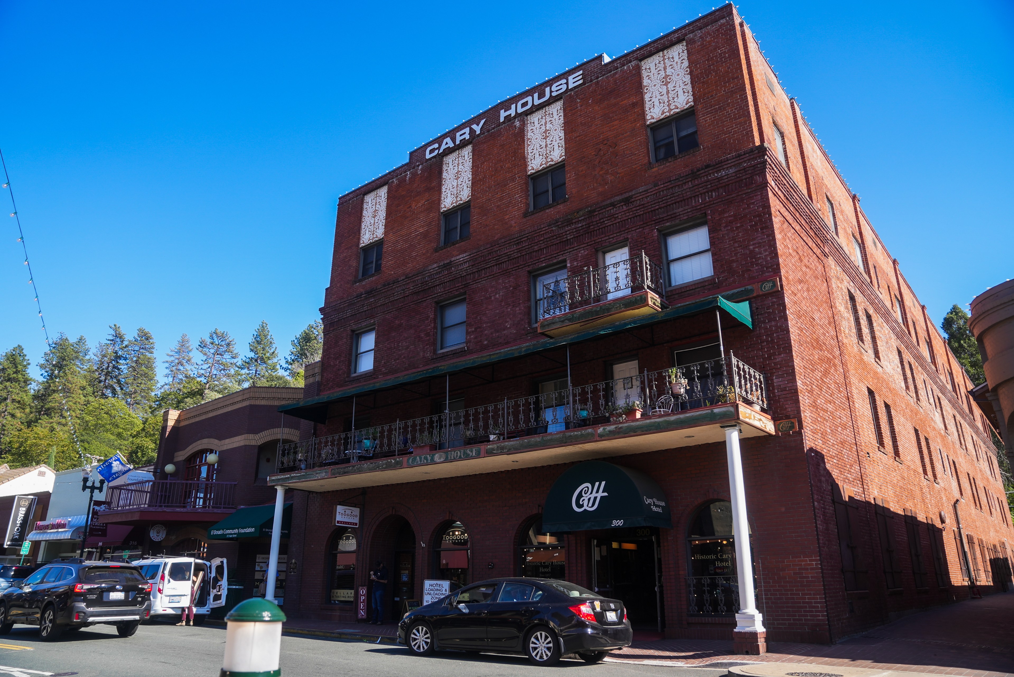 The image shows a historic red brick building called Cary House, featuring balconies and multiple windows. Cars are parked on the street below it.