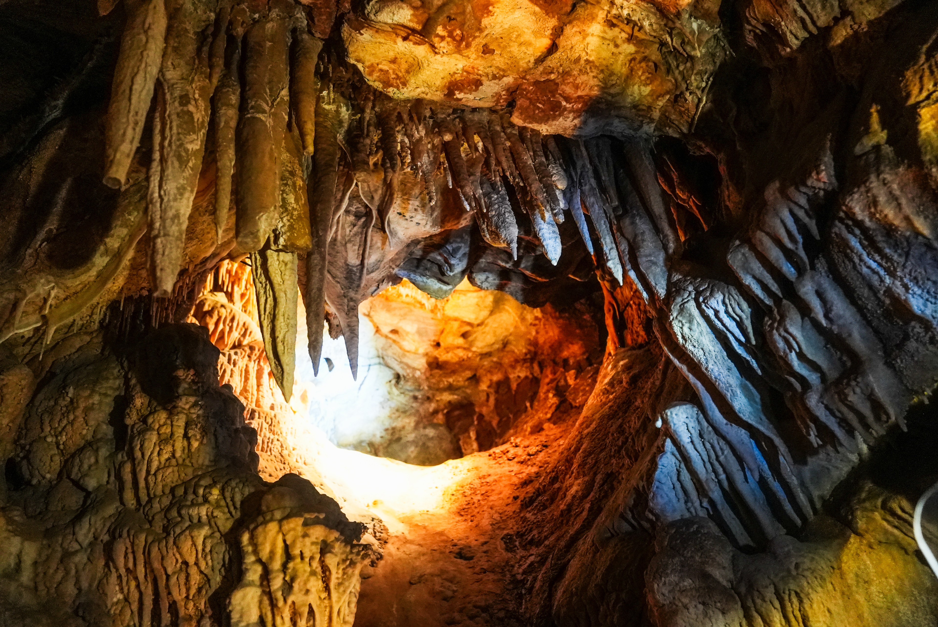 A vibrant cave interior shows pointed stalactites hanging from the ceiling. The scene is illuminated with warm orange and cool blue lights, highlighting rough textures.