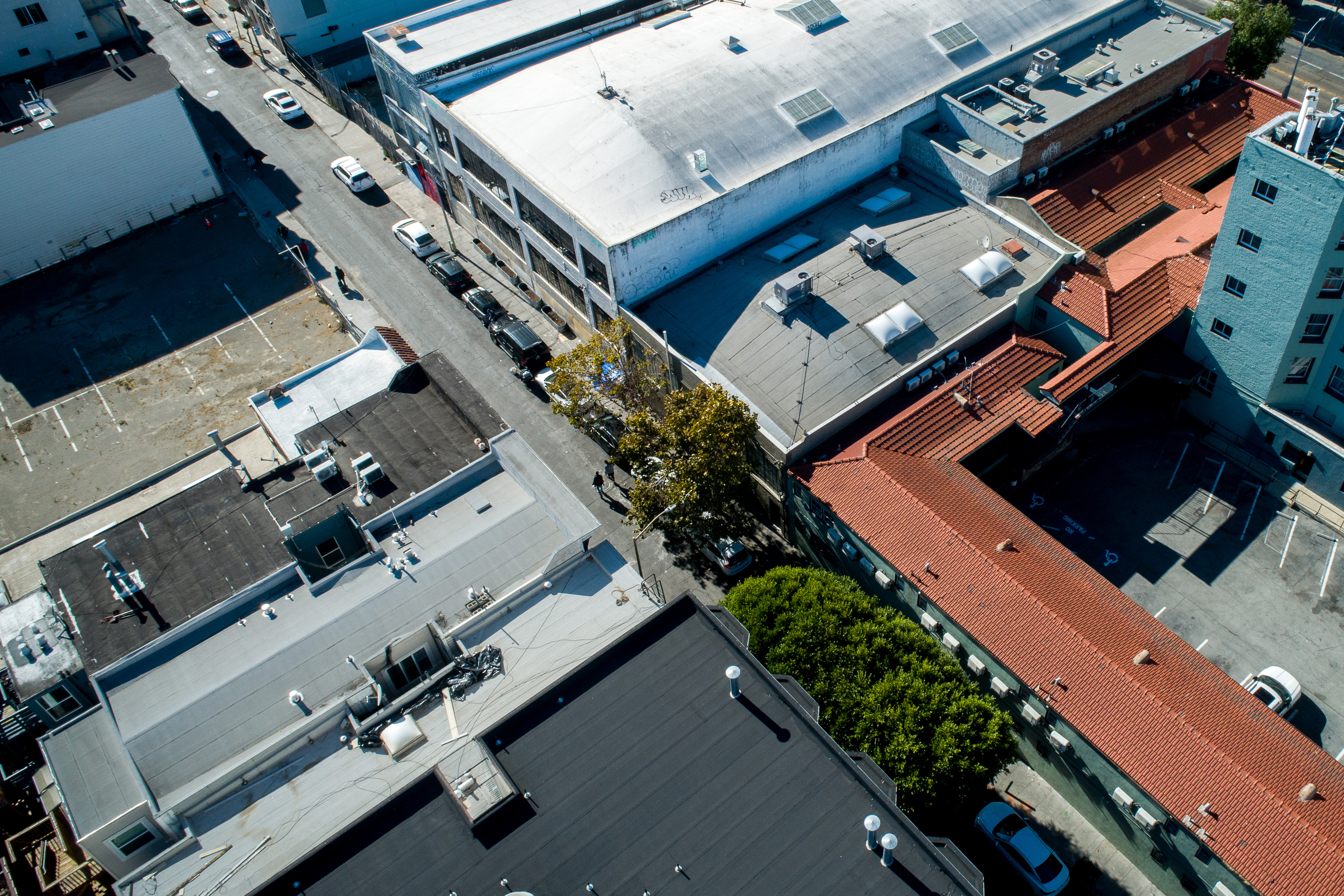 The image shows a bird's-eye view of a city block with buildings, streets, and parking areas. Trees and parked cars line a narrow street.