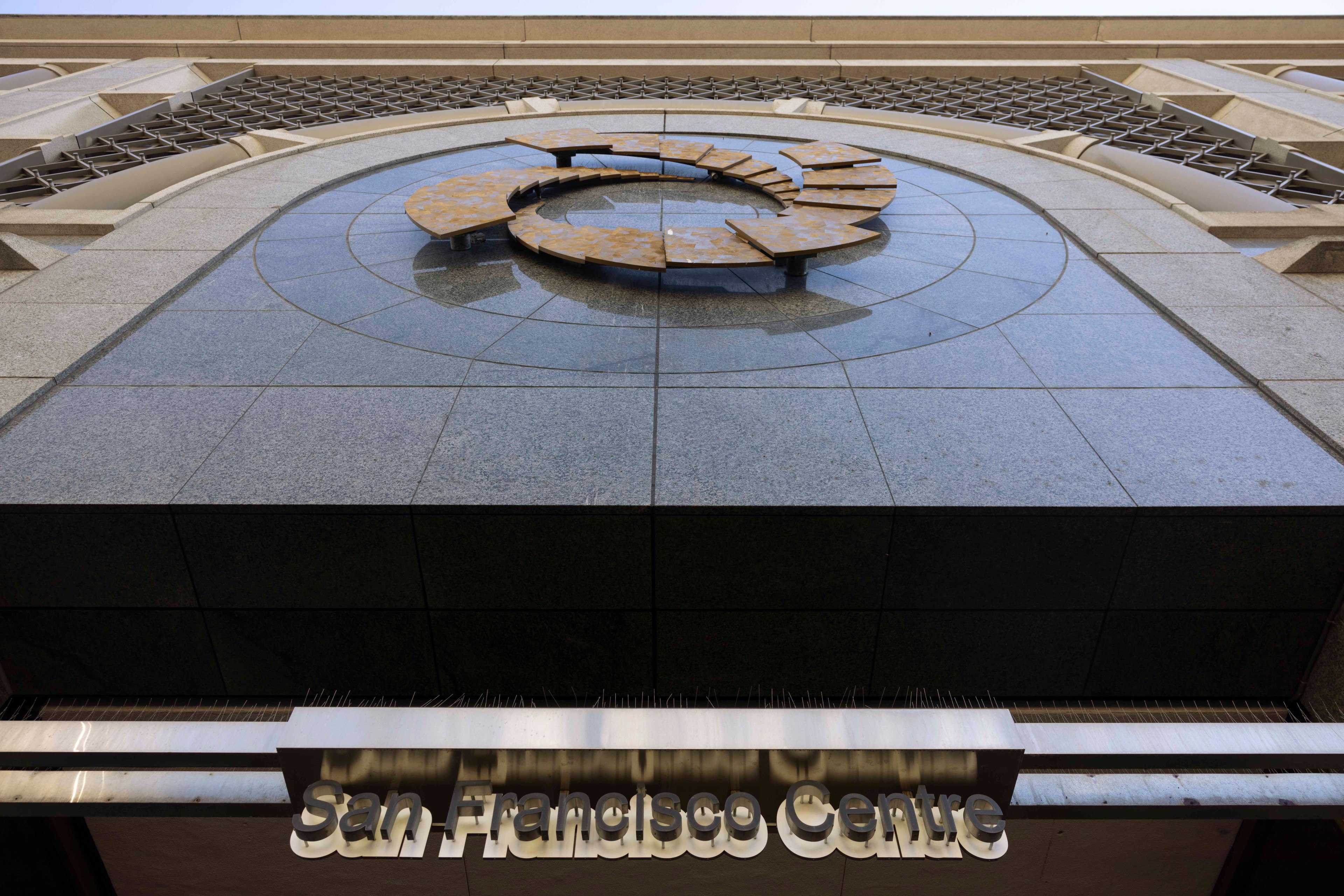 The image shows the exterior of a building with the name &quot;San Francisco Centre&quot; beneath a circular architectural feature on a tiled wall.