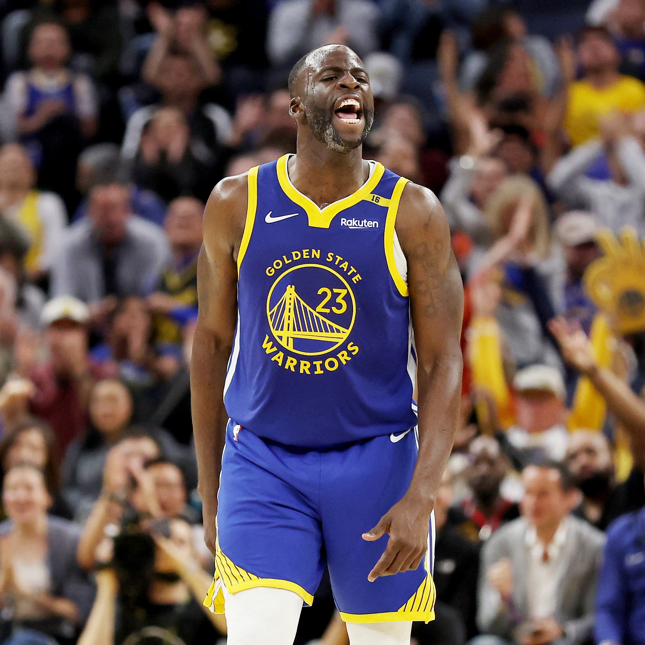 A basketball player in a Golden State Warriors jersey is on the court, yelling in excitement. The crowd behind him is cheering enthusiastically.