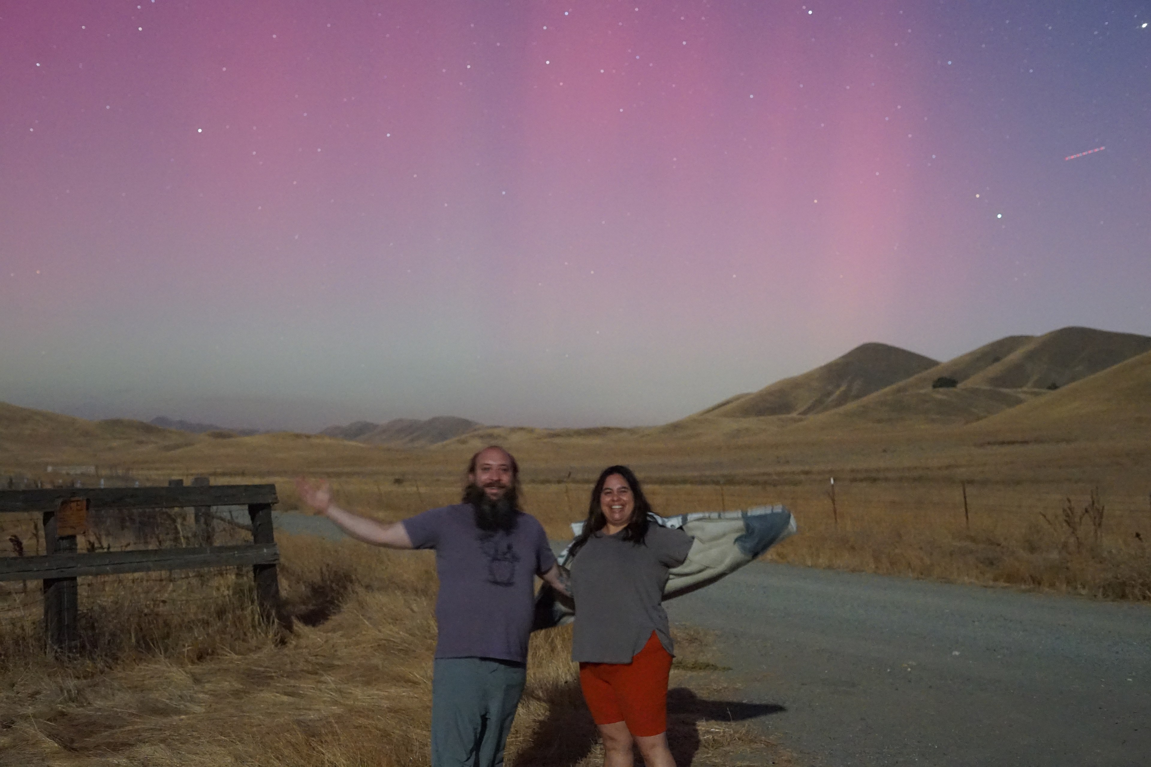 A man and woman stand near a road beneath a dazzling sky showing the aurora borealis in rural Northern California.