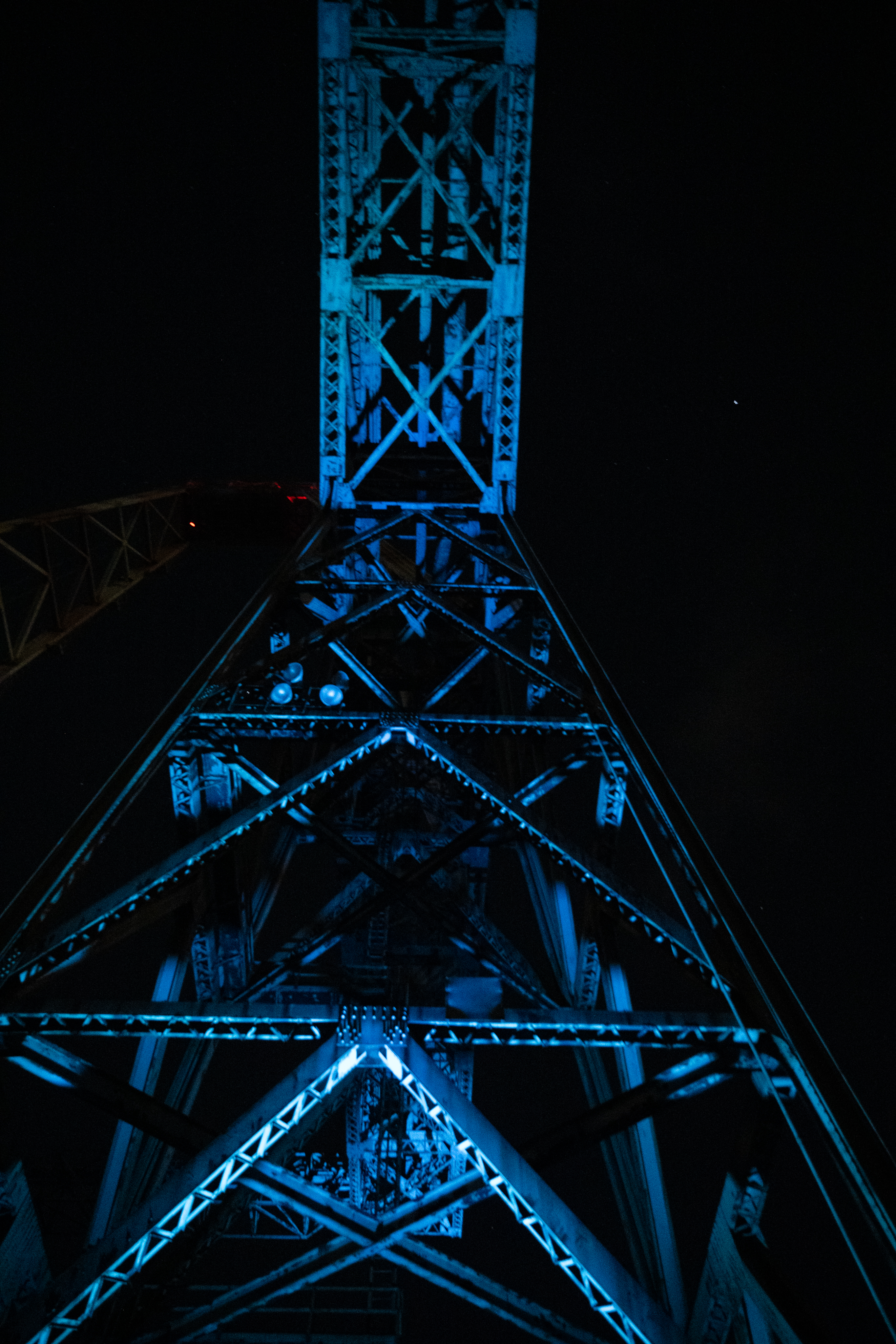 A metallic tower illuminated with blue lights stands stark against the dark night sky, showcasing its intricate crisscross lattice structure.