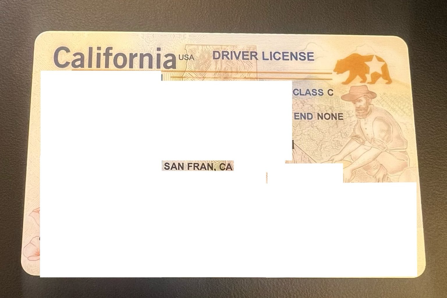 The image shows a California driver's license with personal details obscured, featuring a bear and a man in a hat in the background.