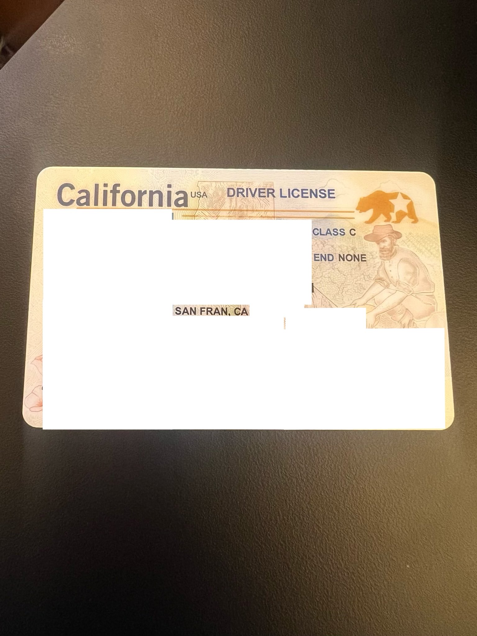 The image shows a California driver's license with personal details obscured, featuring a bear and a man in a hat in the background.