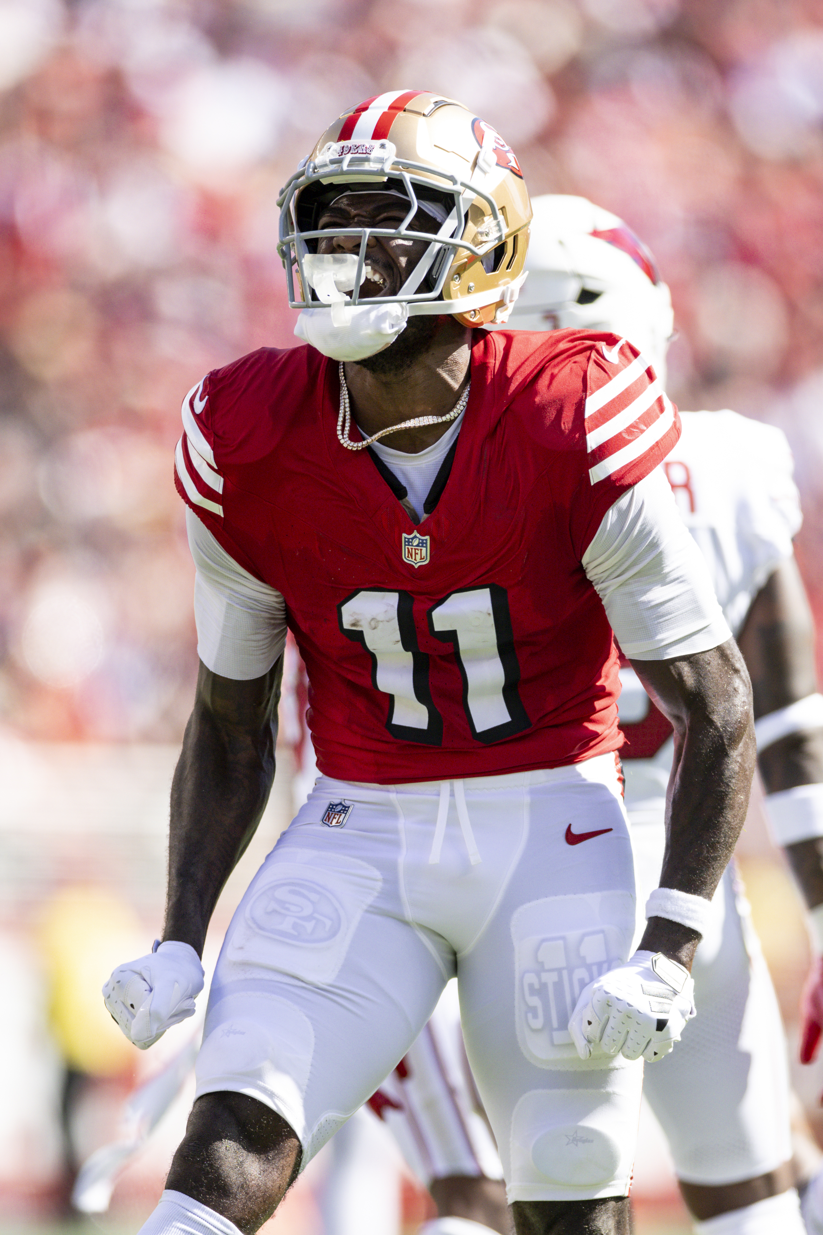 A football player wearing a red jersey with the number 11 and gold helmet shouts in excitement on the field. He has white gloves and white pants.