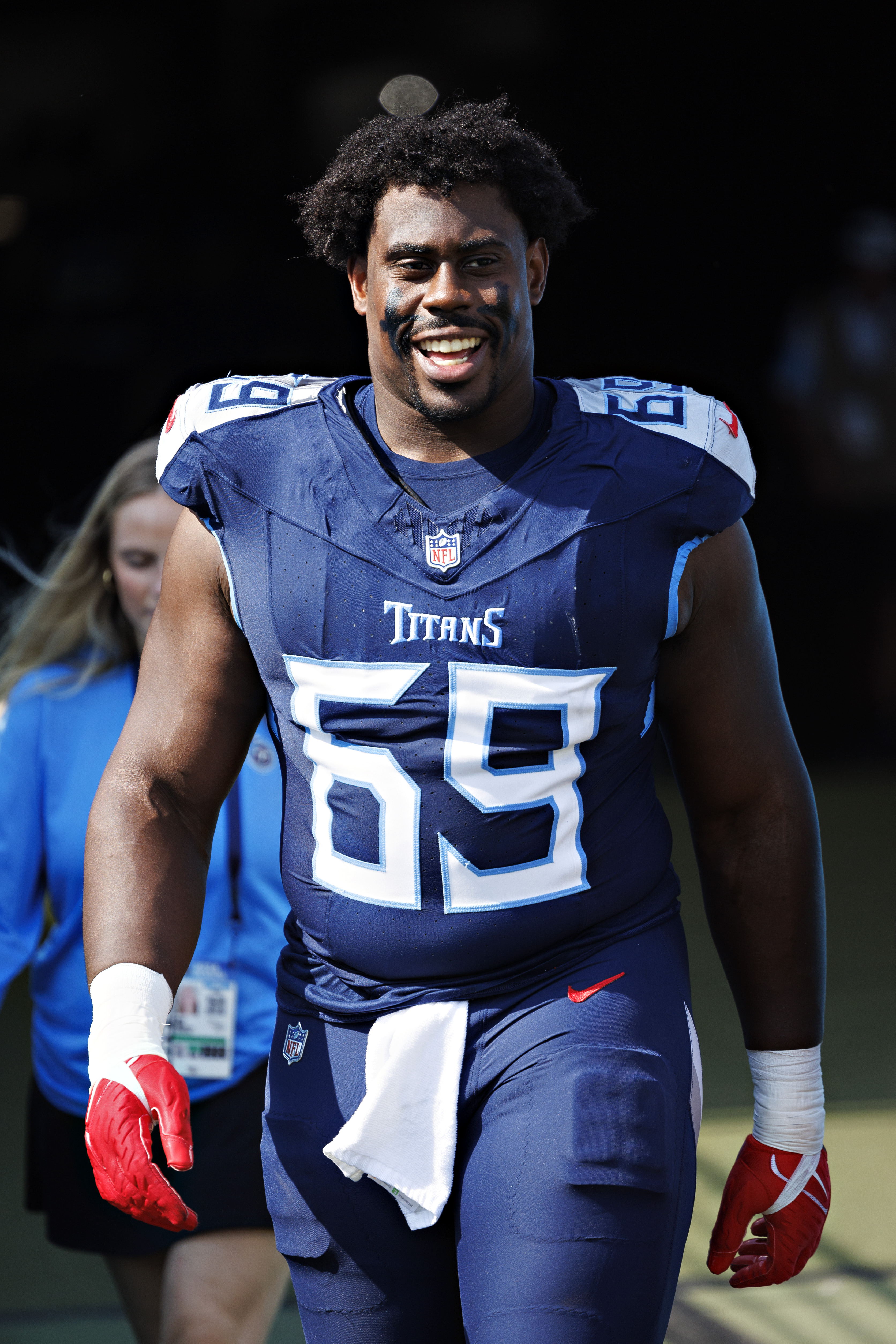 A football player in a navy blue Titans uniform smiles broadly. He wears a number 69 jersey and red gloves, with eye black under his eyes.